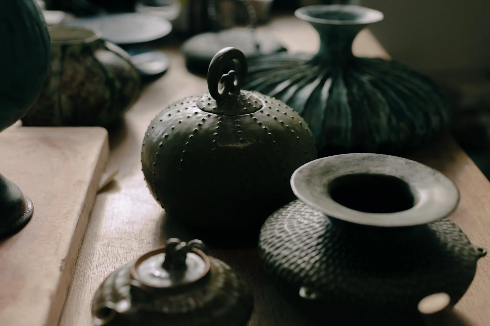 Assorted green-colored ceramic vases, including a small teapot with a handle, on a wooden table.
