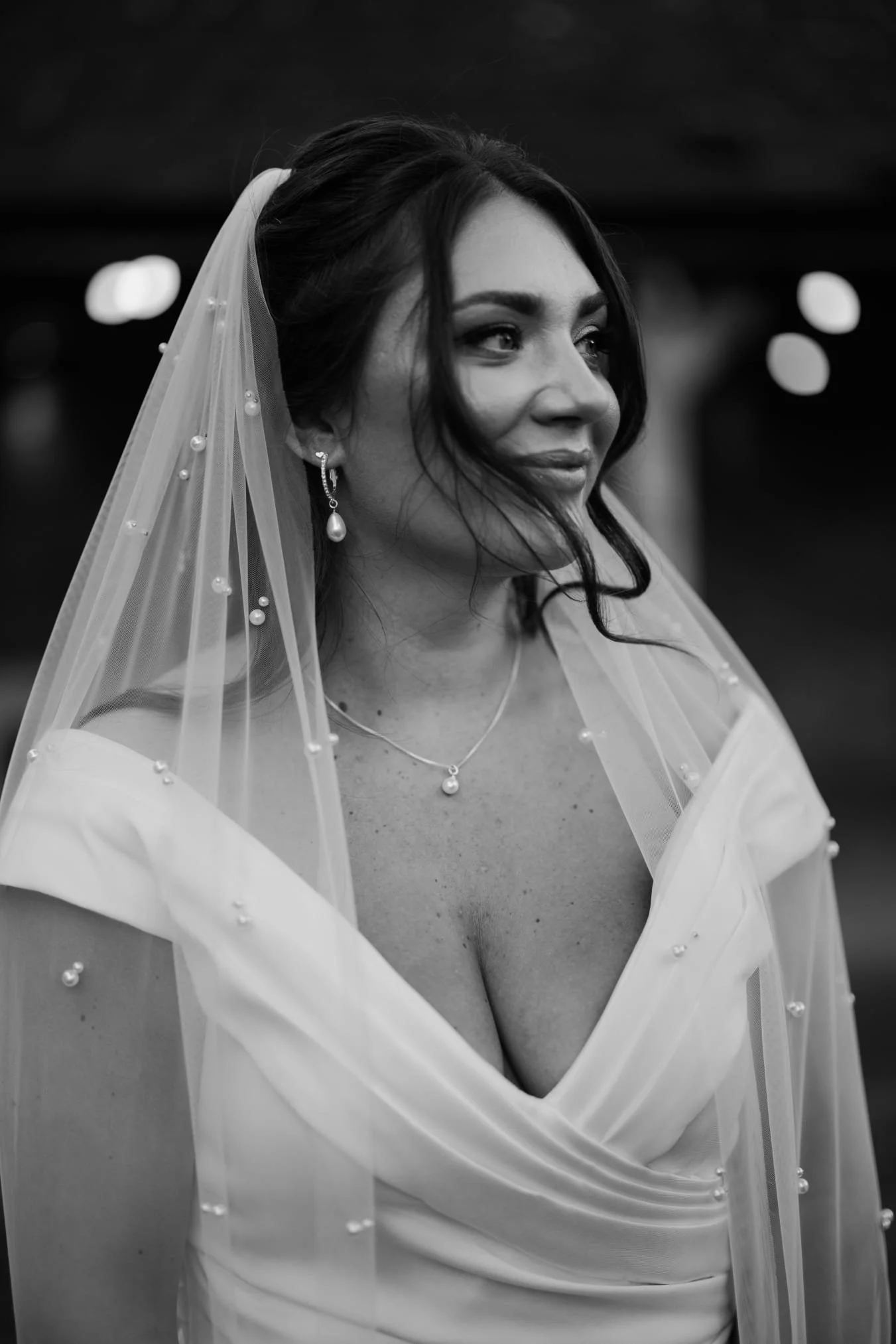 A woman wearing a wedding dress and veil, looking to her left with a slight smile, in black and white.