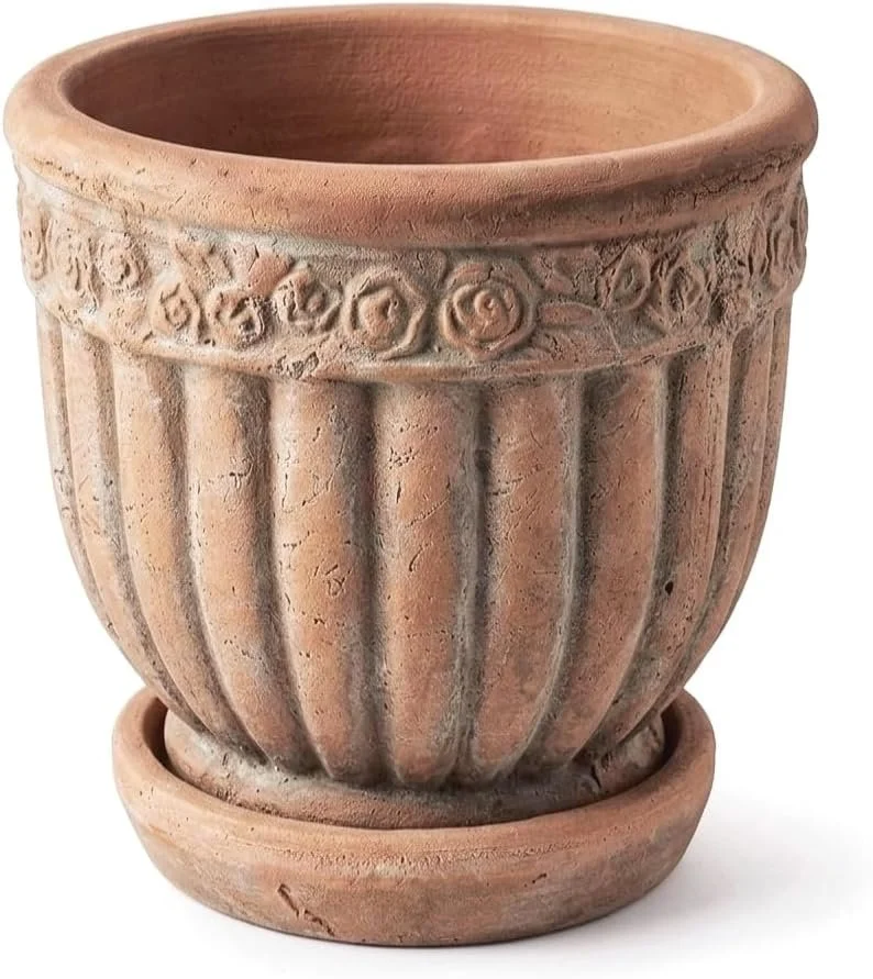 A terracotta flower pot with decorative carved patterns around the upper rim and vertical ridges on the sides, placed in a matching saucer.