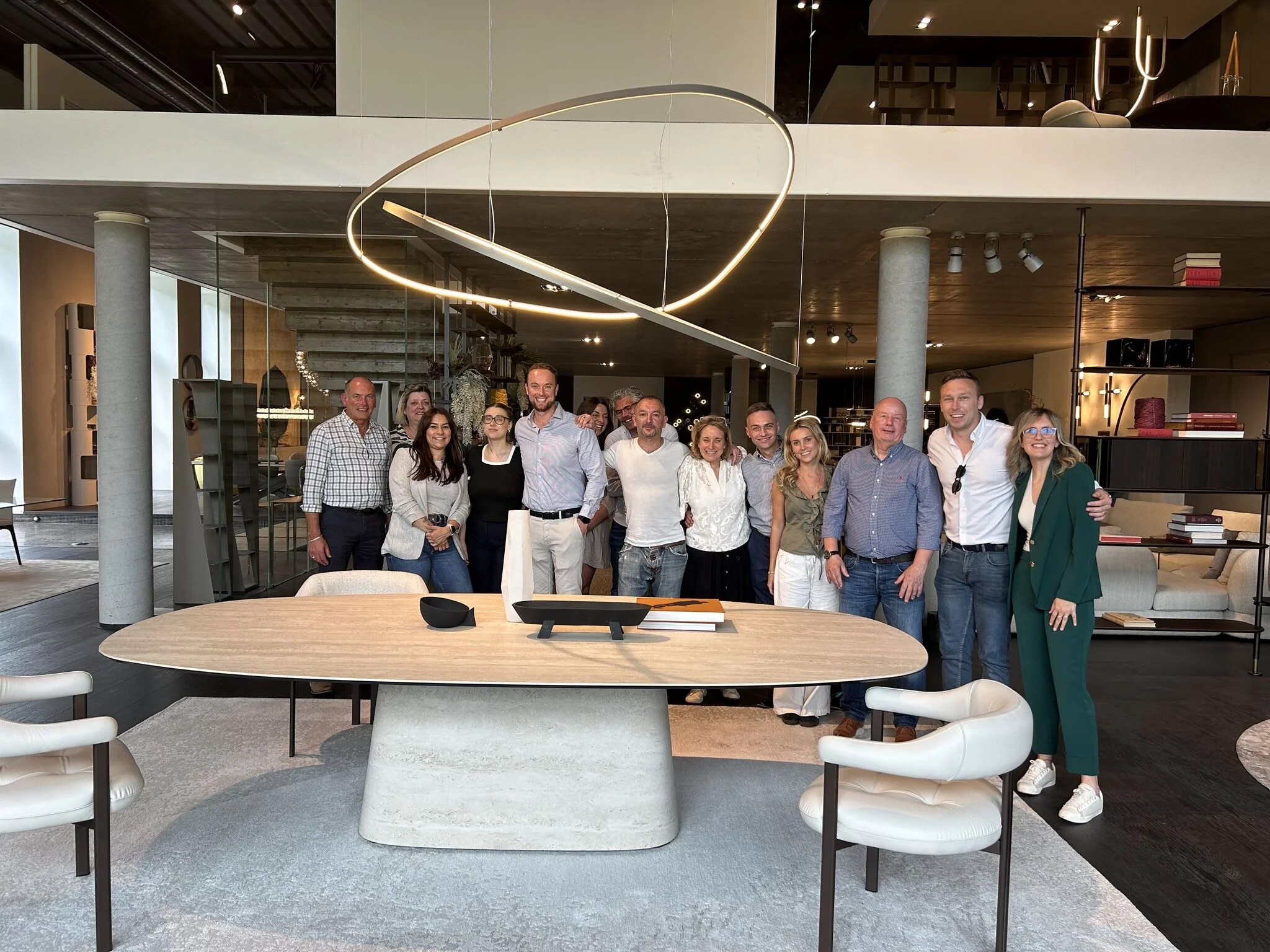 Group of 15 people standing together in a modern, stylish living room or office space, smiling and posing for a photo.