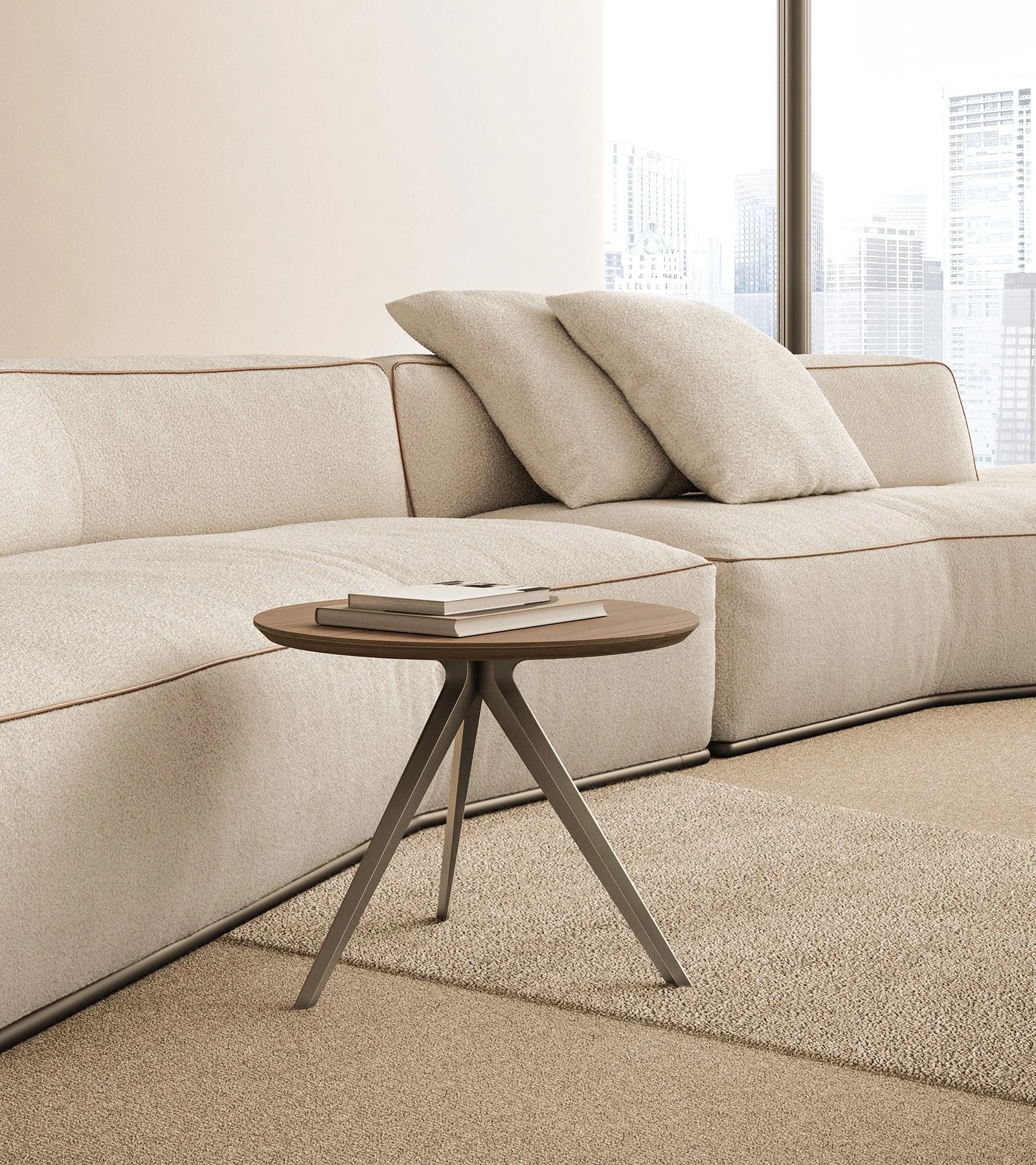 Modern living room with a beige sectional sofa, two beige throw pillows, a small round wooden side table with a few books on it, and large windows showing a cityscape in the background.