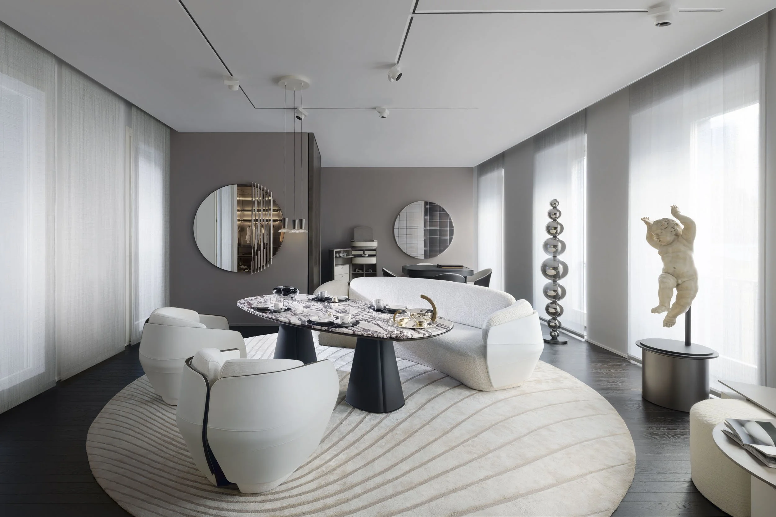 Modern dining room with a marble table, white and oval-shaped chairs, a plush white sofa, decorative sculptures, mirrors, and large windows with sheer curtains.
