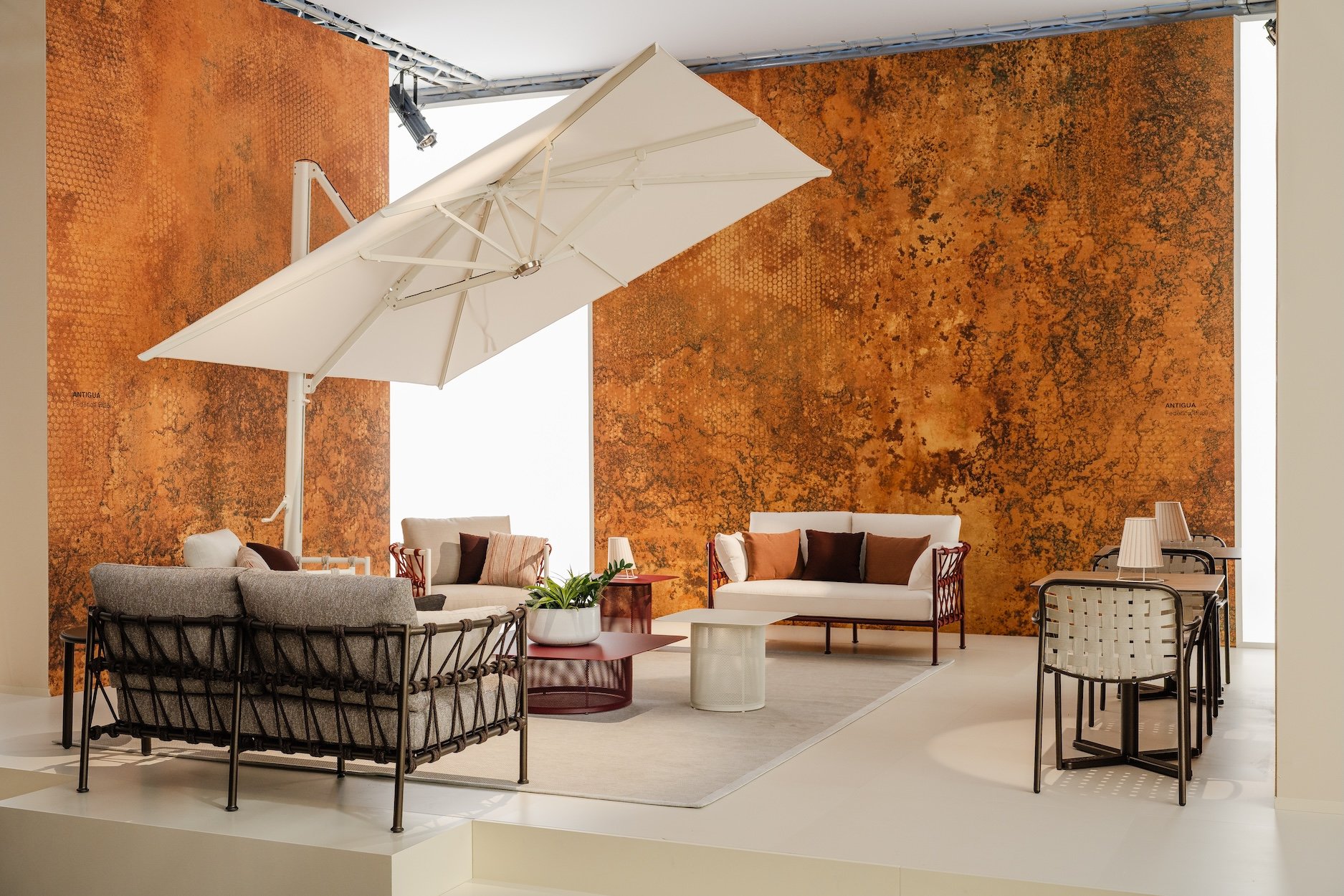 Modern lounge area with beige, brown, and gray furniture, a large cream-colored umbrella, and textured orange wall background.