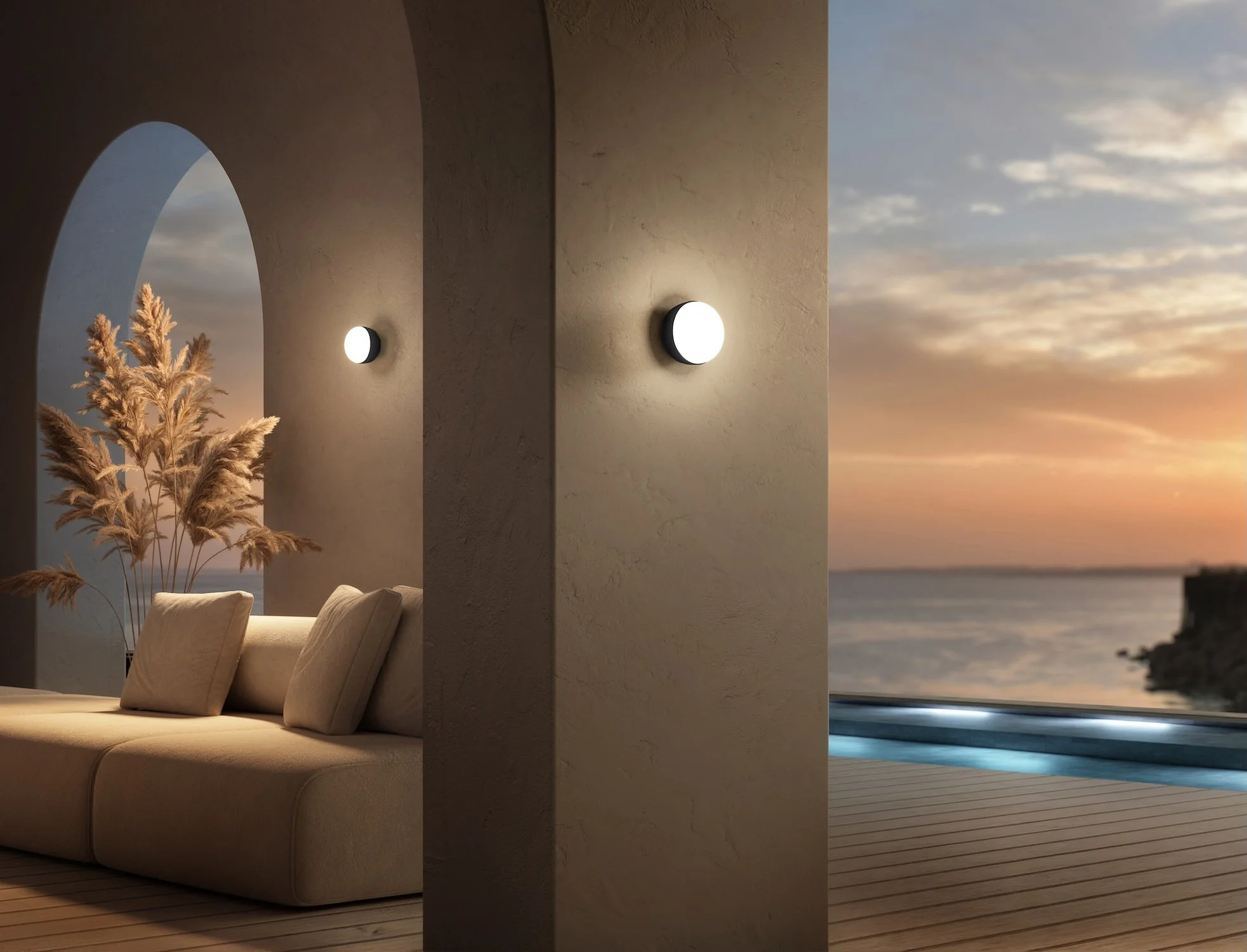 A modern outdoor patio area with a couch and decorative plants, overlooking a sunset over water, with a pool nearby.