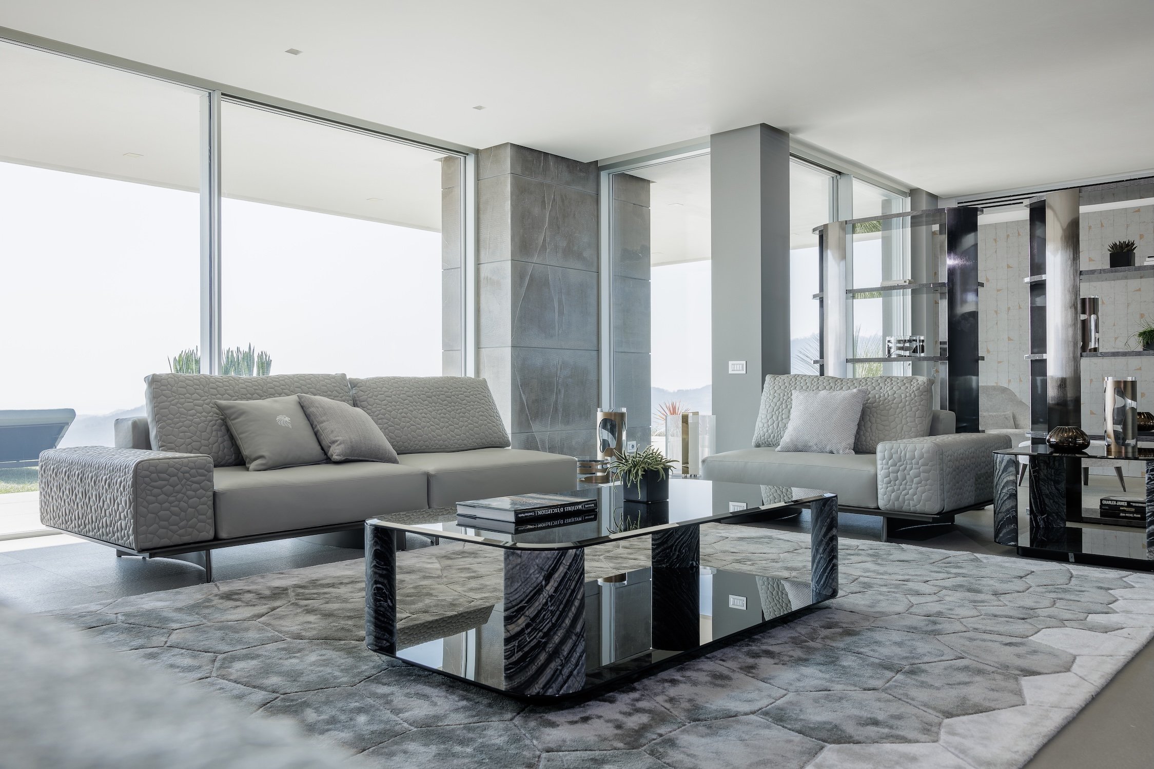 Modern living room with two light gray sofas, a black marble coffee table, large windows, and decorative items.