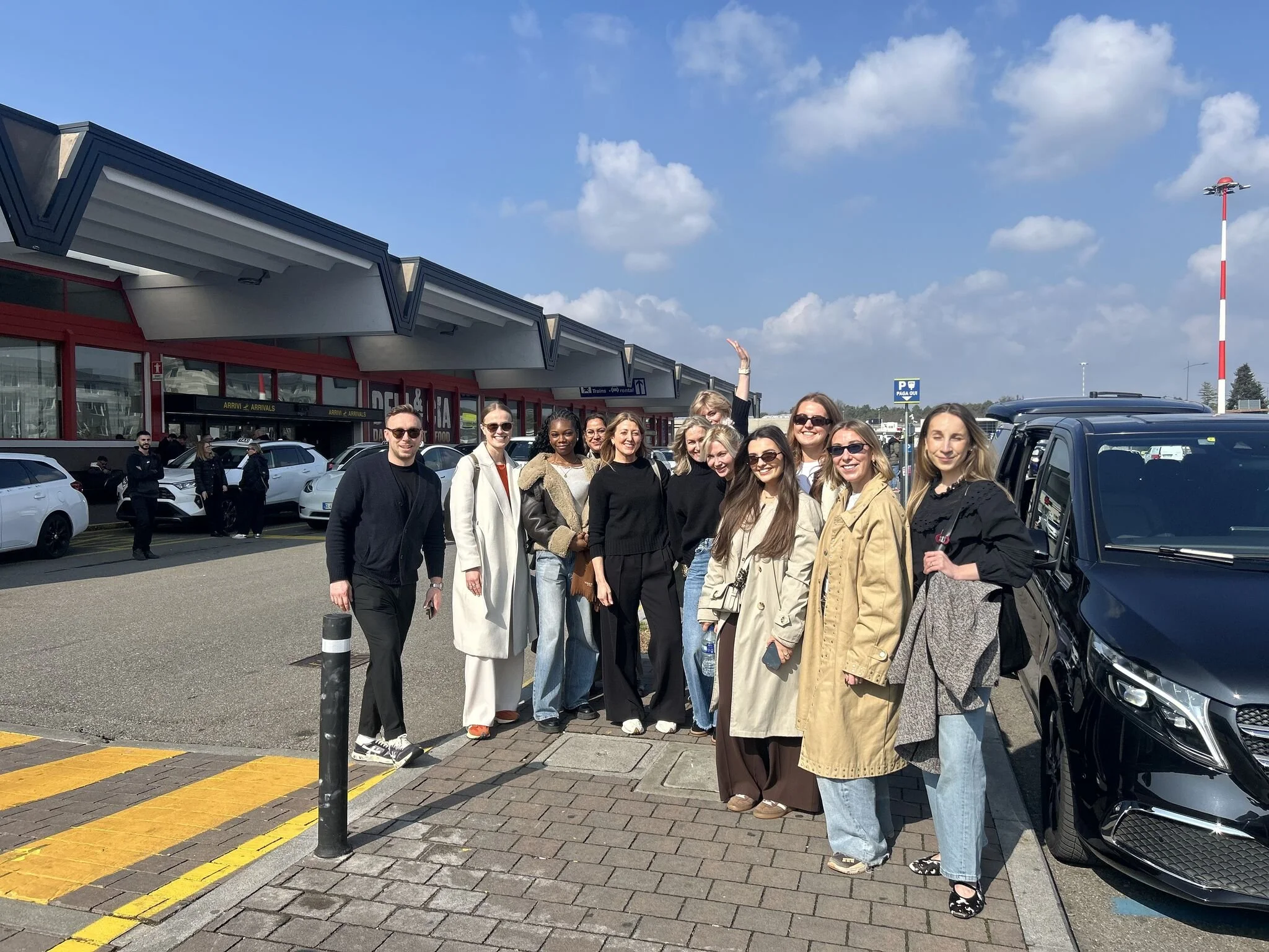 Group of people standing outside of a building at an airport on a sunny day.