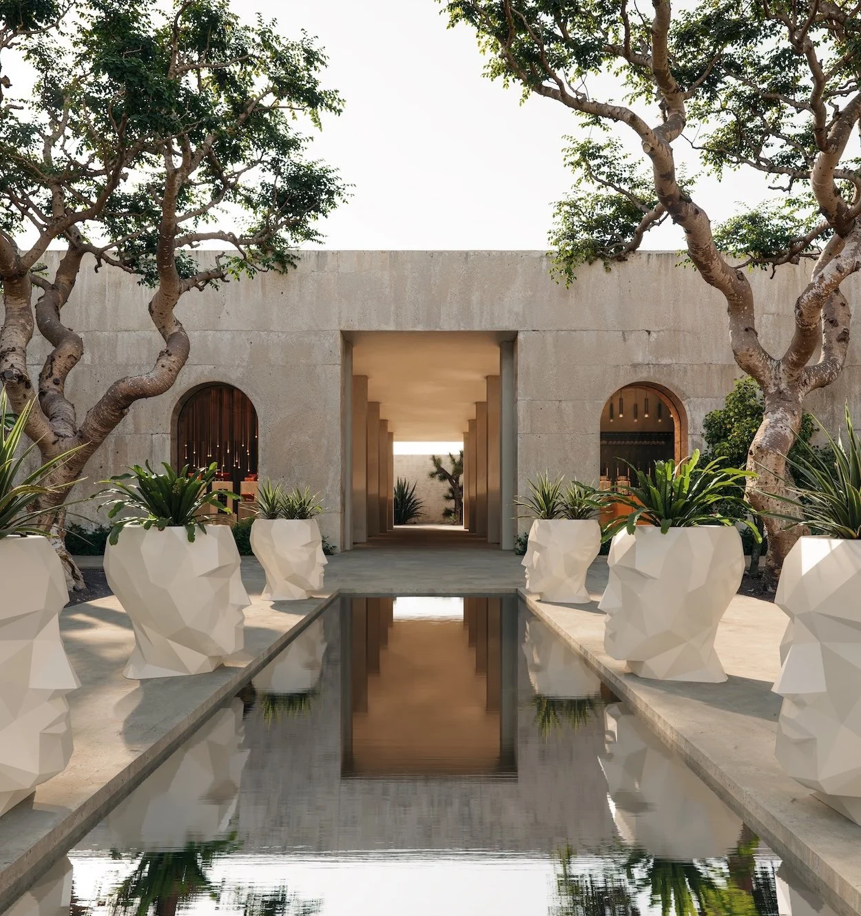 Modern courtyard with a water feature flanked by white geometric planters shaped like human faces, trees, and a concrete building with arched windows and a colonnaded walkway.