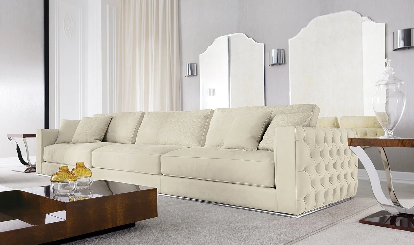 A living room with a beige, tufted sofa, glass and wood coffee table, and mirrored wall panels.