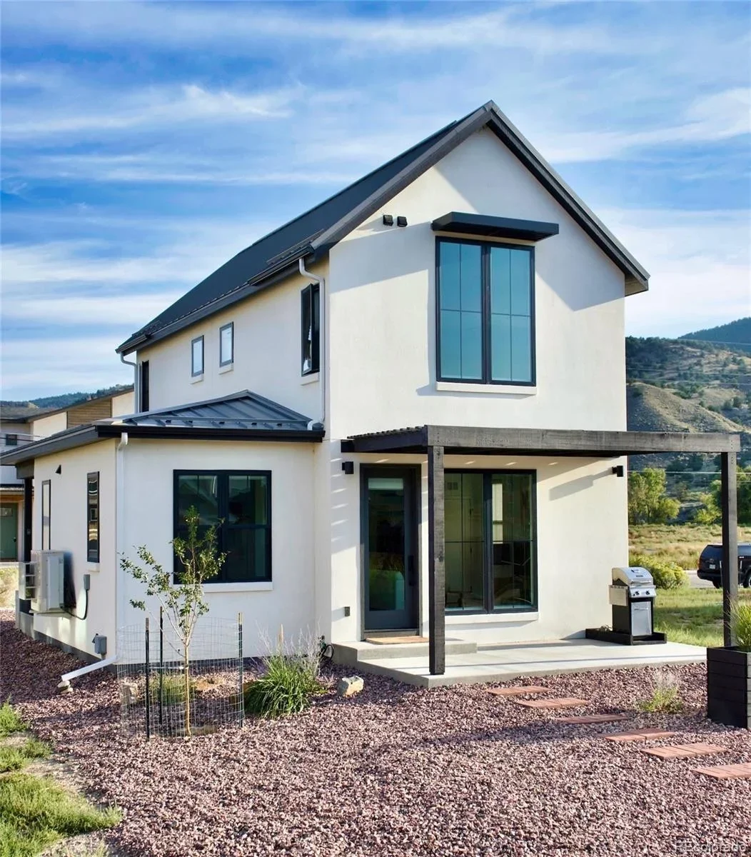 Modern two-story house with white exterior, large windows, black accents, and a small front yard with gravel and plants.
