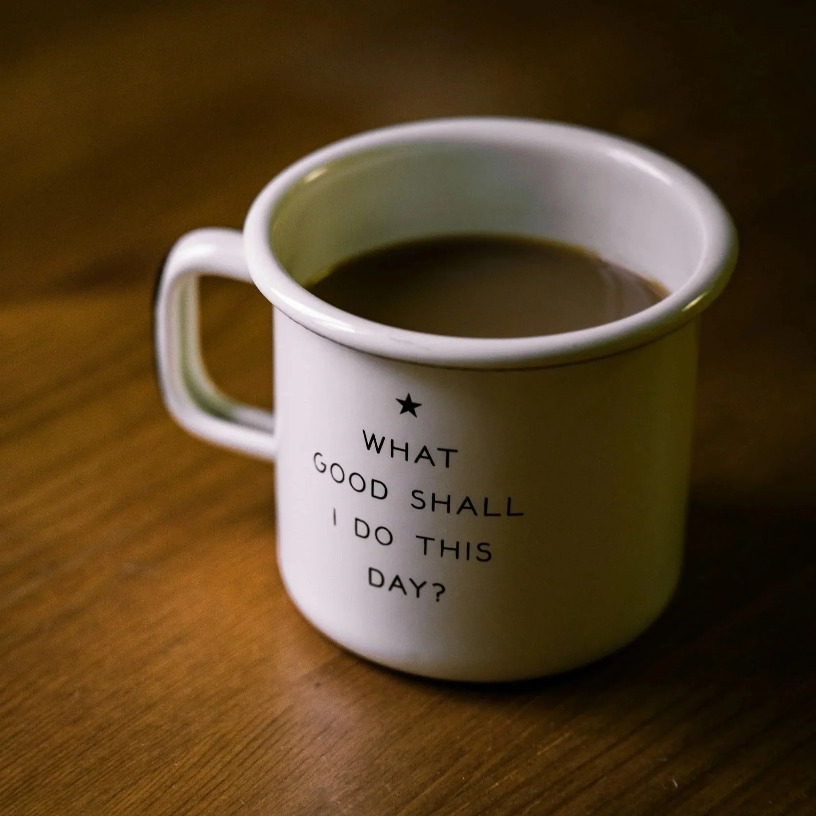 White mug with black text on a wooden surface, containing coffee or tea
