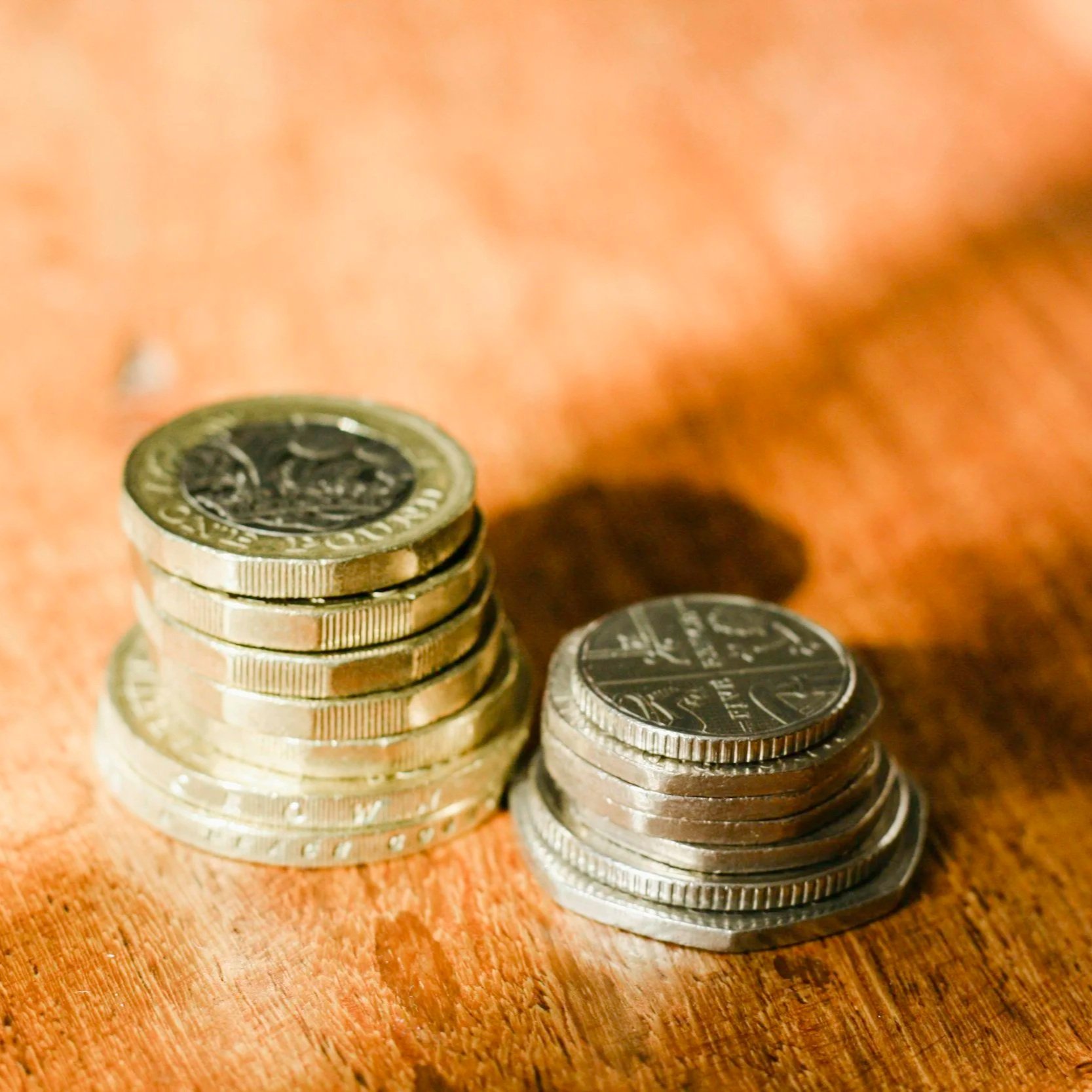 Close-up of two stacks of US coins on a wooden surface, with one stack taller than the other.