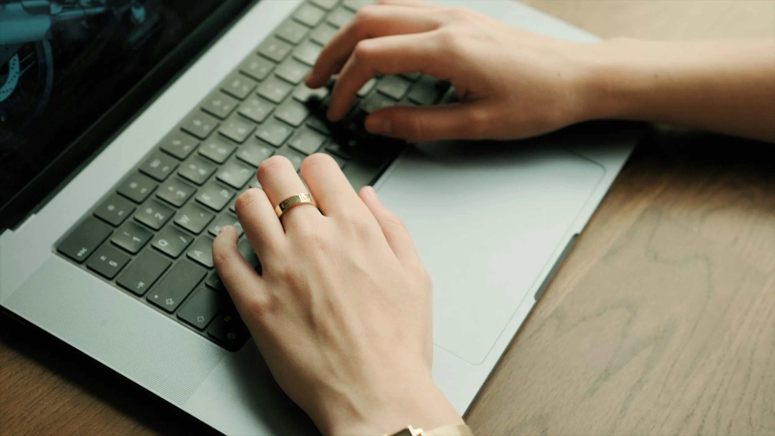 Close-up of hands typing on a silver laptop keyboard, with a wooden surface underneath.