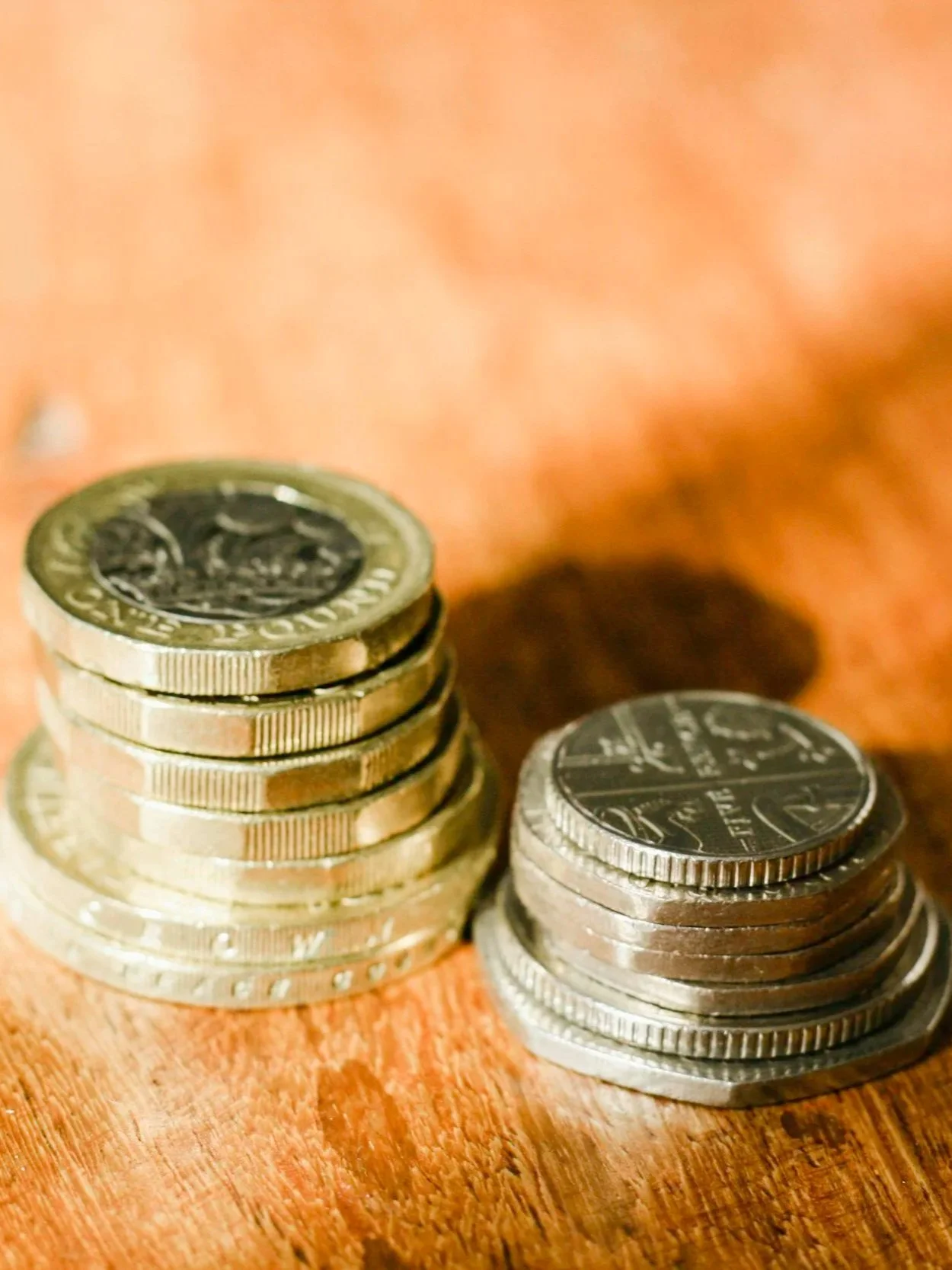 Two stacks of U.S. coins on a wooden surface, one stack taller than the other, with a blurred background.