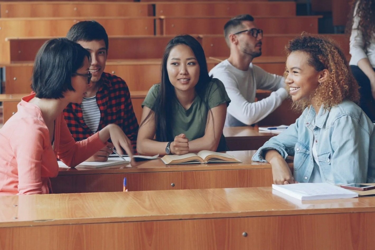 A diverse group of five college students sitting in a lecture hall, engaging in conversation and studying together.
