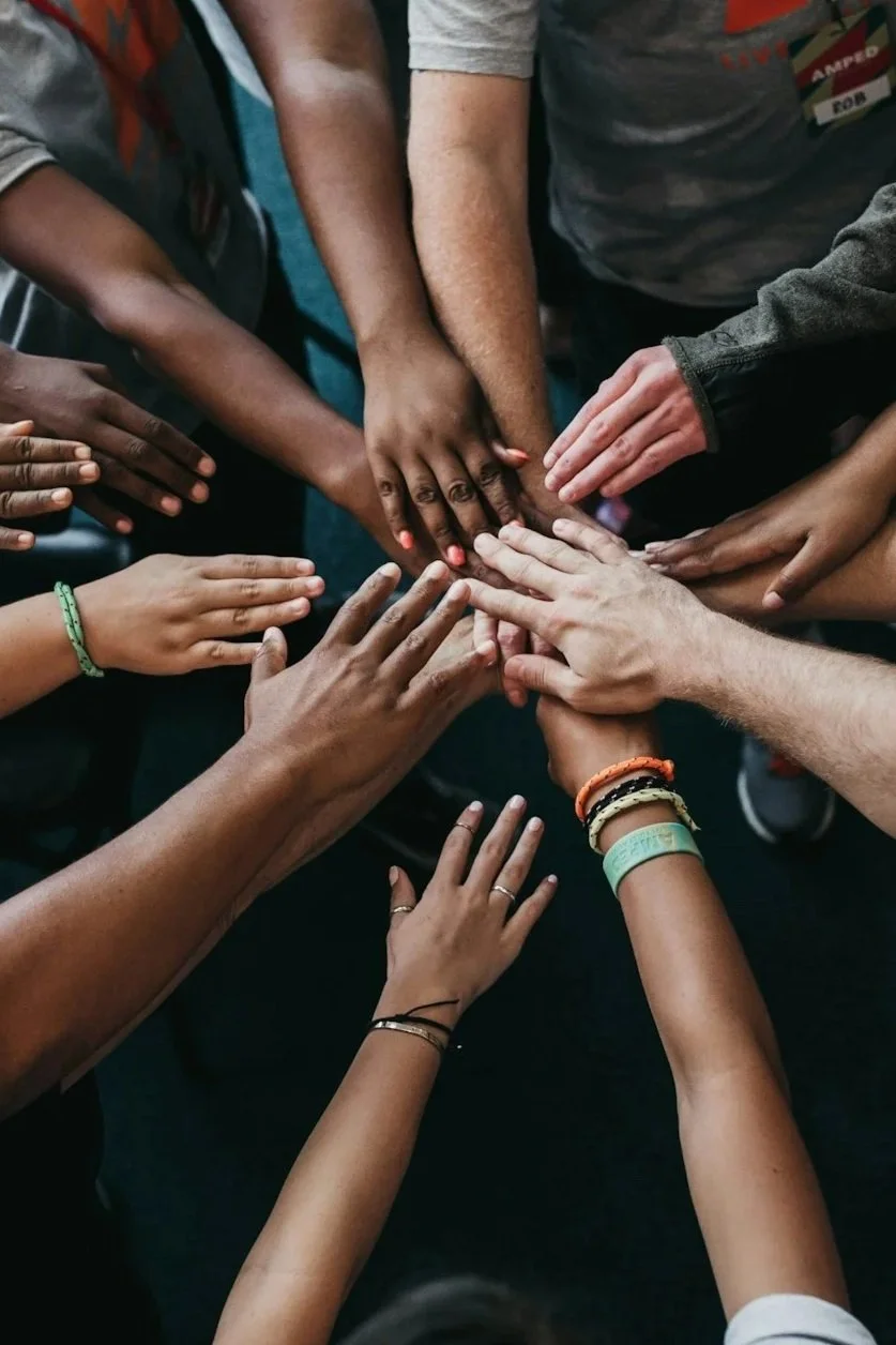Multiple hands of diverse individuals stacked together in a circle with palms touching, symbolizing unity and teamwork.