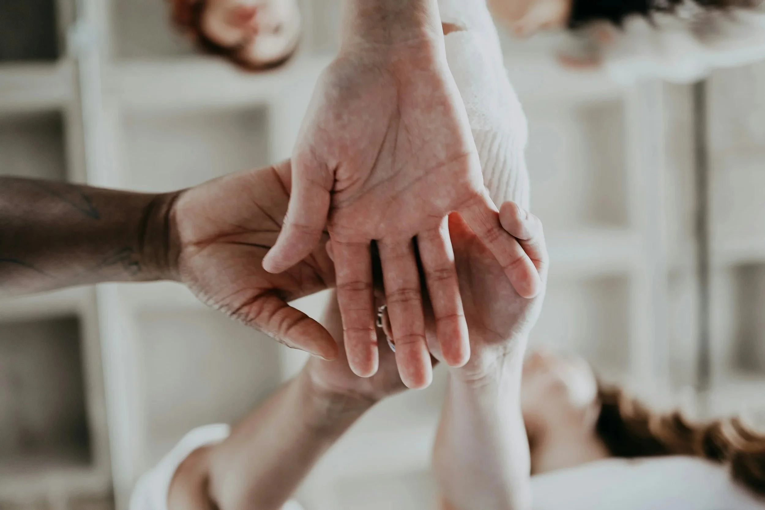 Close-up of two people holding hands, one person's hand resting on top of the other's in an indoor setting.
