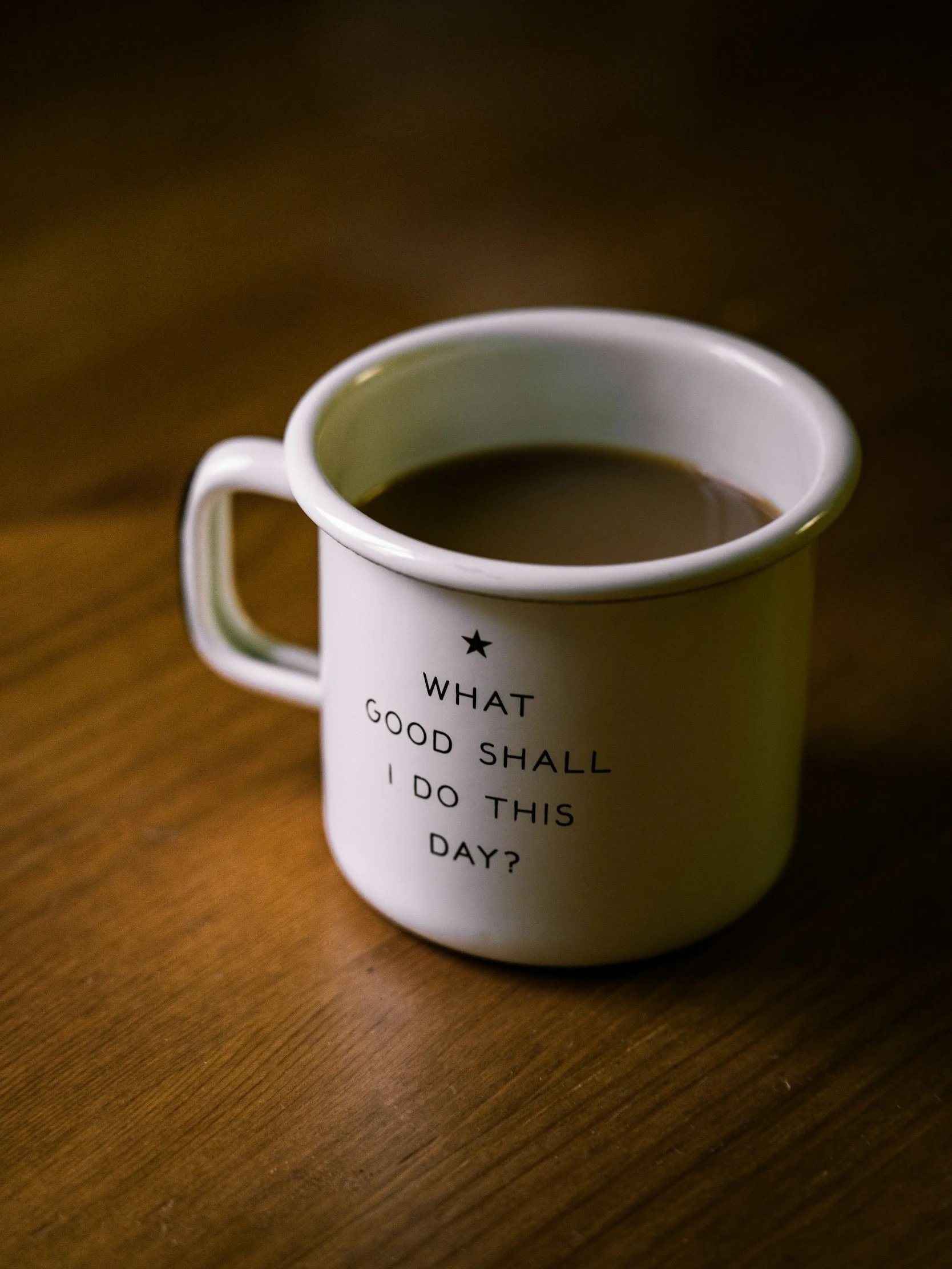A white coffee mug with text on it, sitting on a wooden surface, filled with coffee.