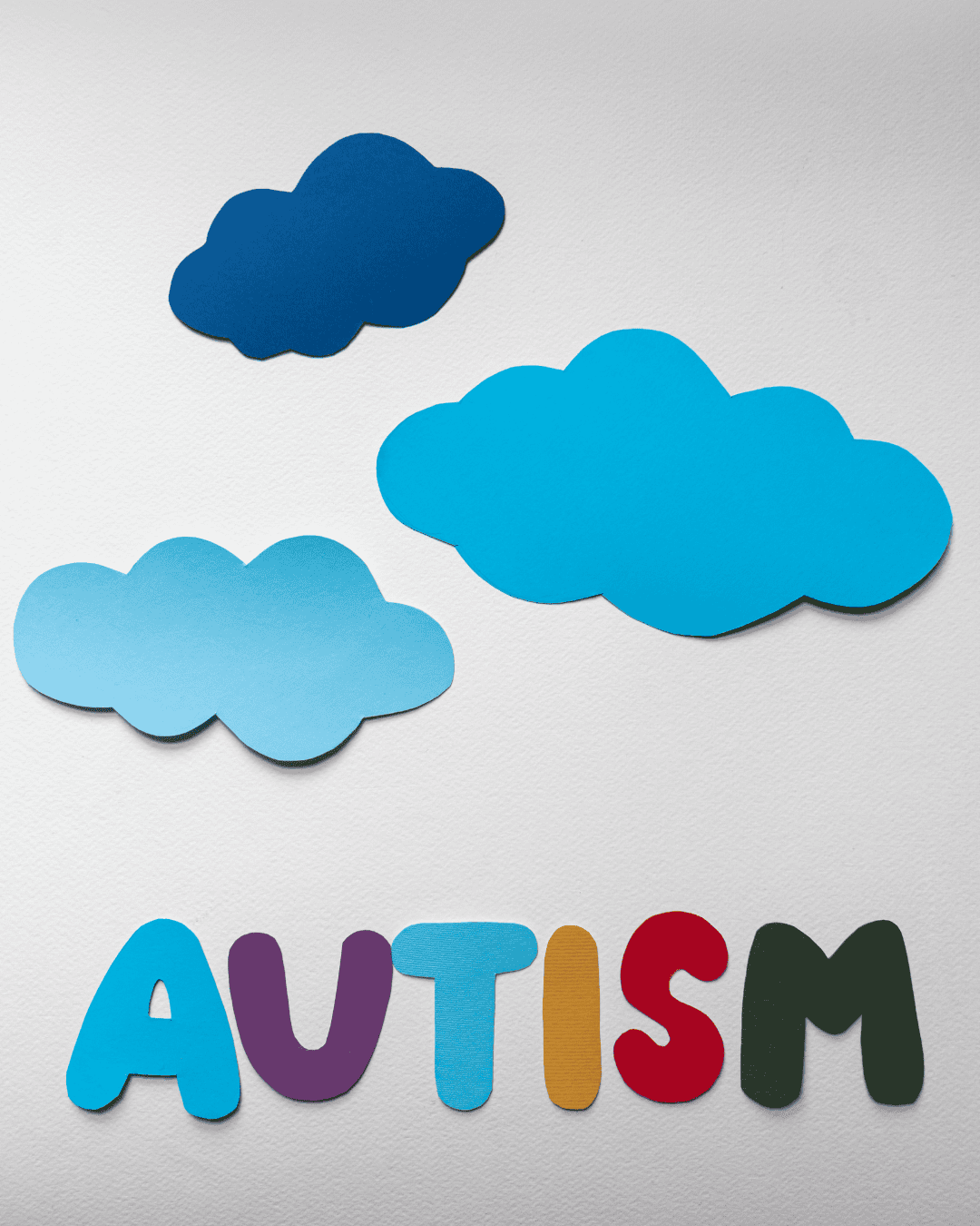 Colorful felt cutouts of four clouds and the word 'AUTISM' in multicolored letters on a white background.