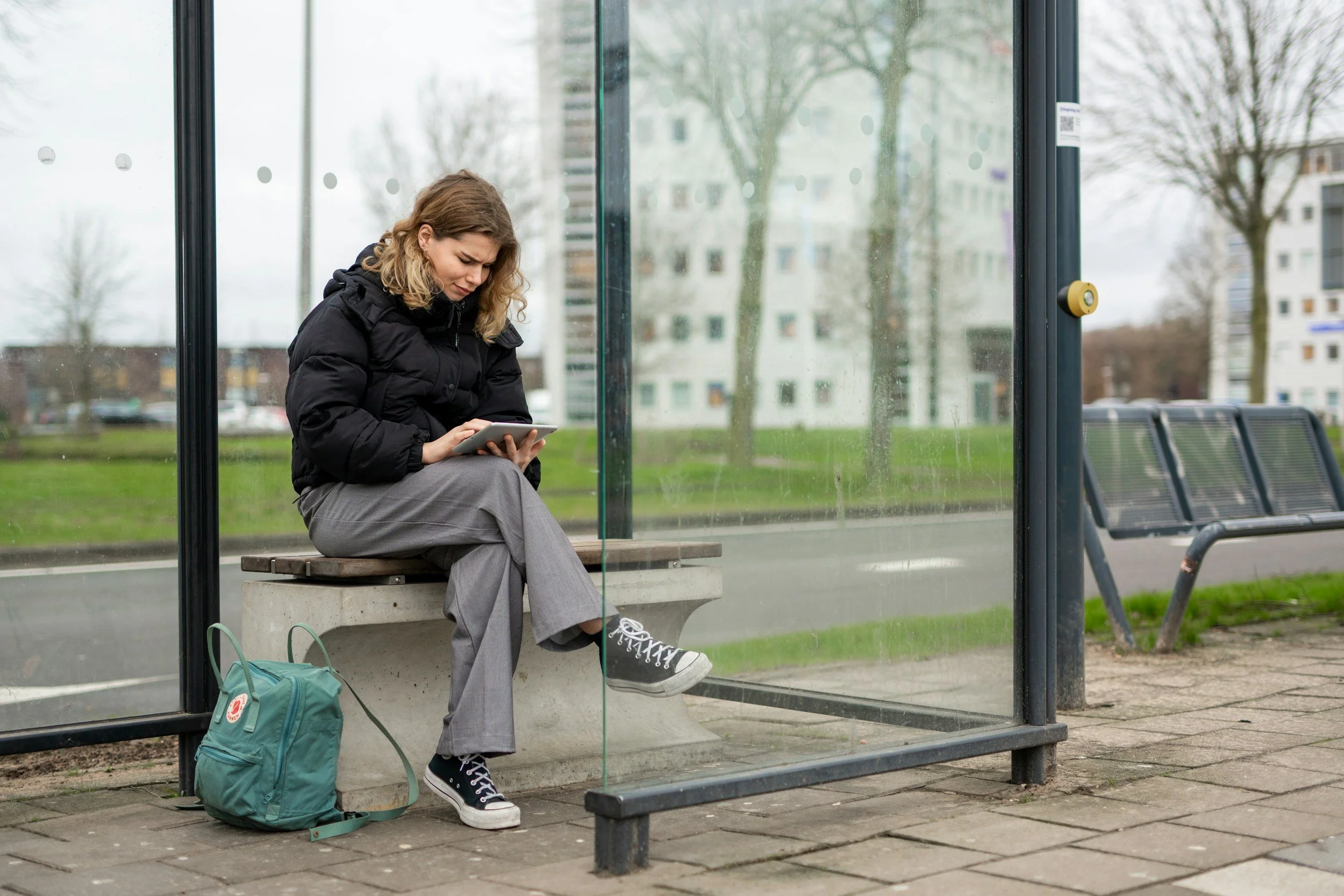 woman sitting at a bus stop looking for information on her tablet