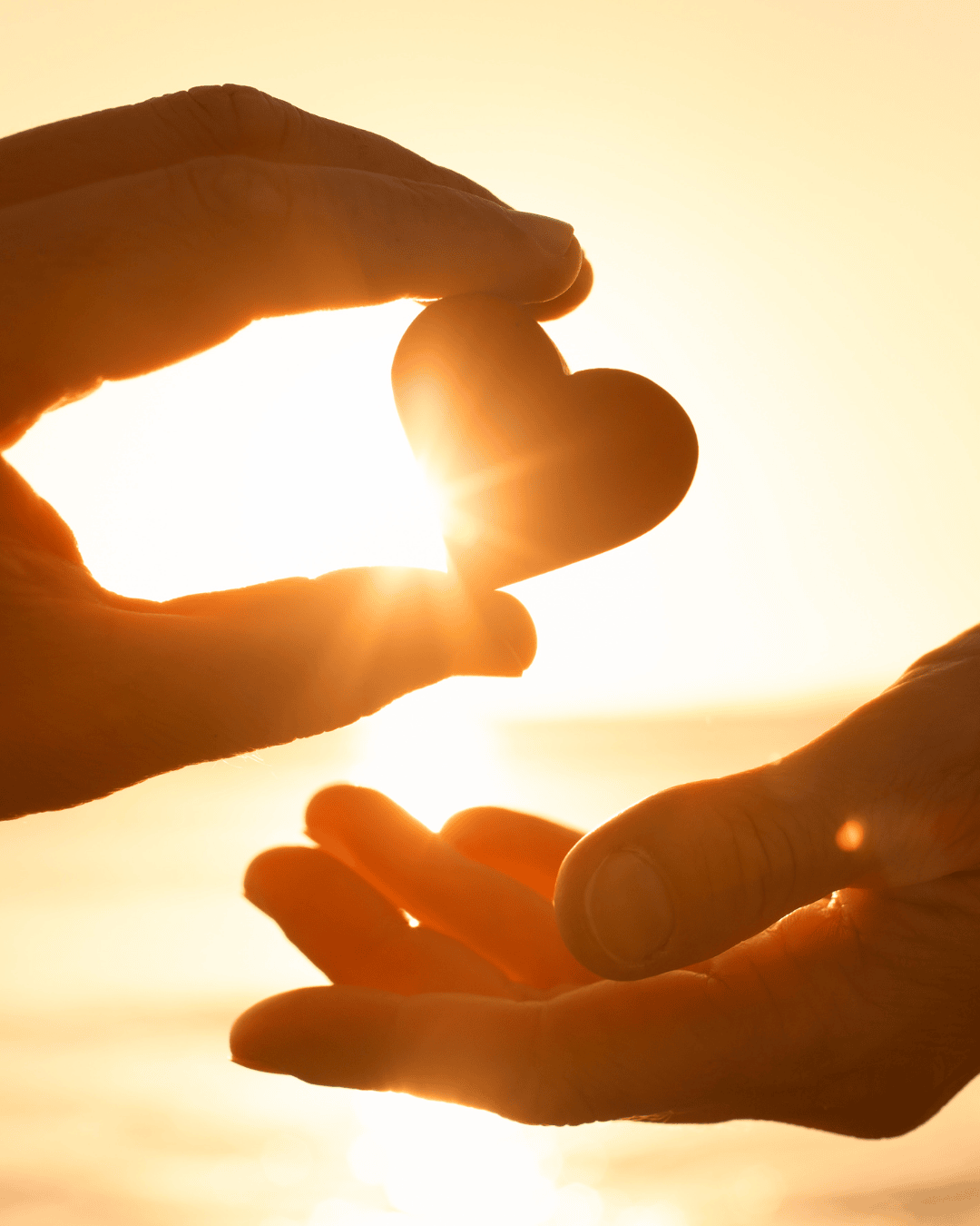 two hands share a wooden heart shape at golden hour