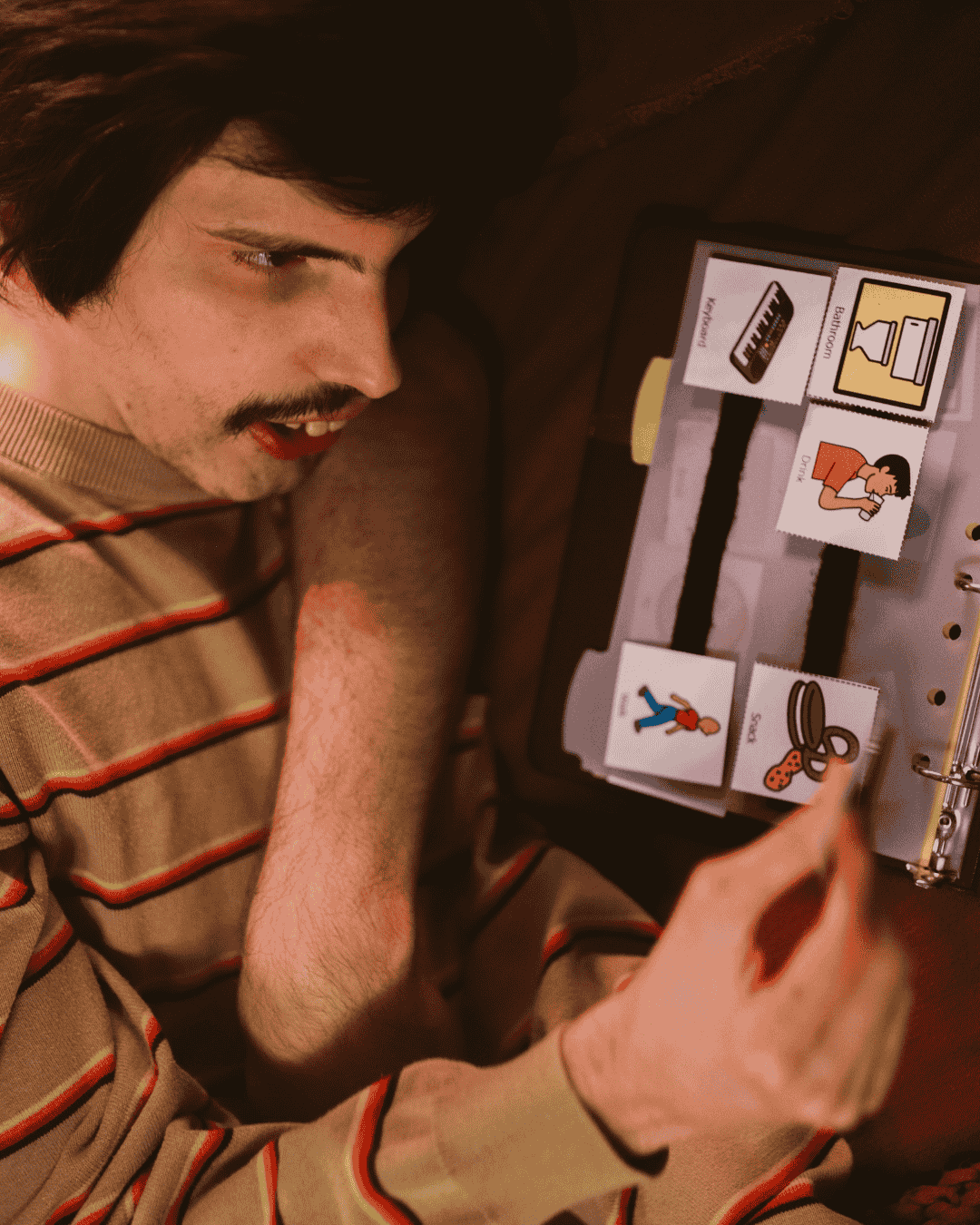 A young man lying on a couch and using an PEC board to communicate