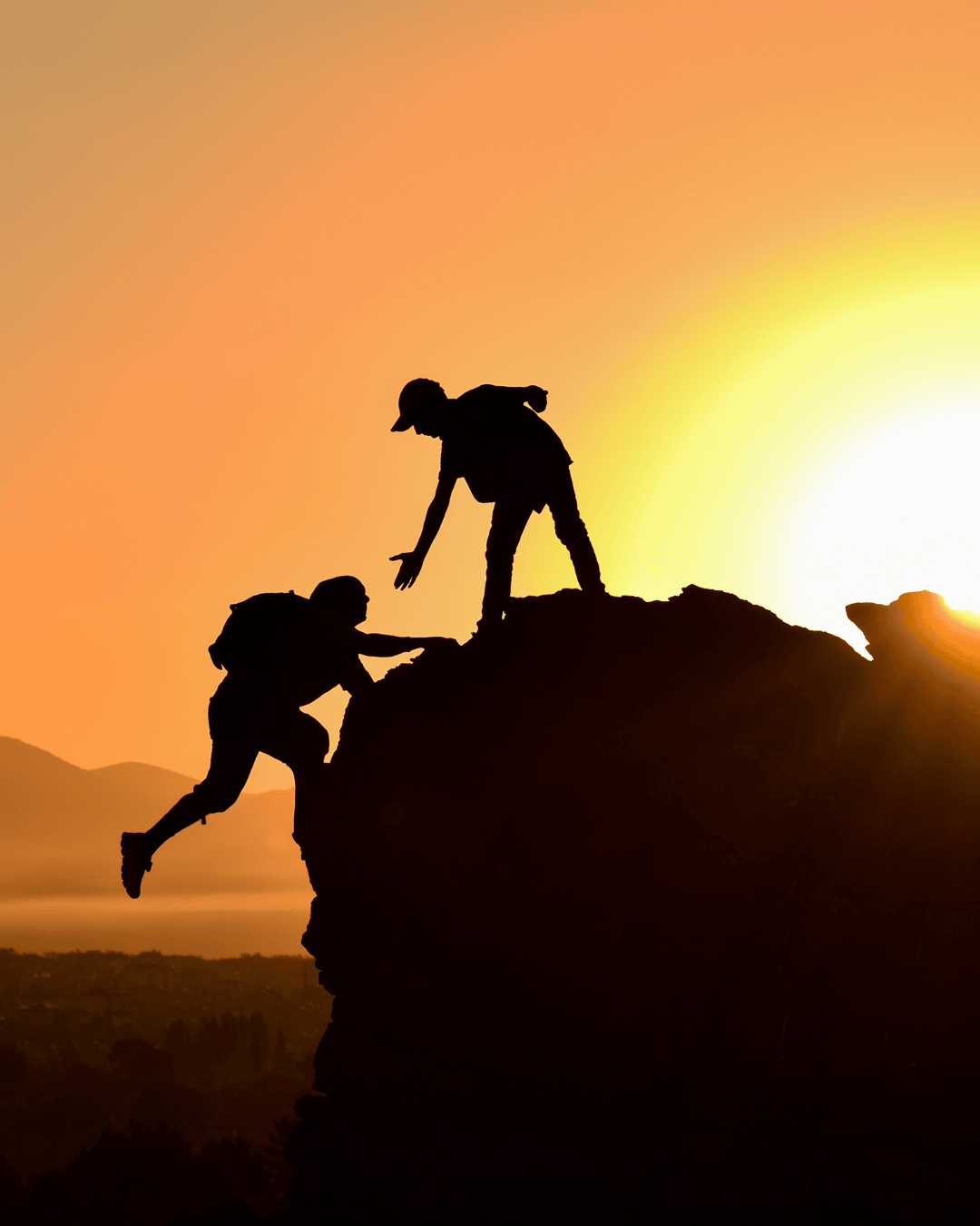 man climbing a mountain and being helped up by another