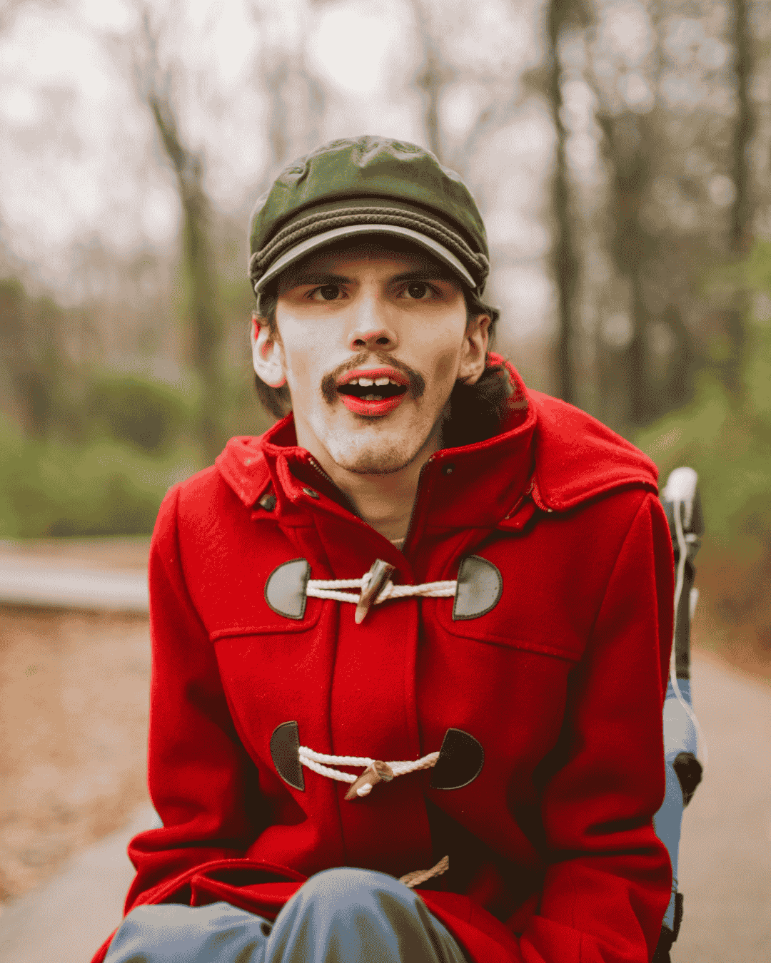 a young man wearing a bright red jacket who has learning disabilities smiles at the camera
