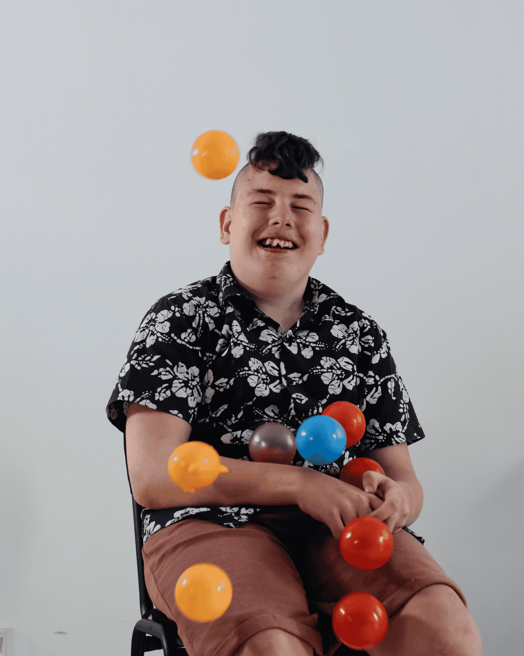 a happy boy smiles as colourful plastic balls are thrown towards him