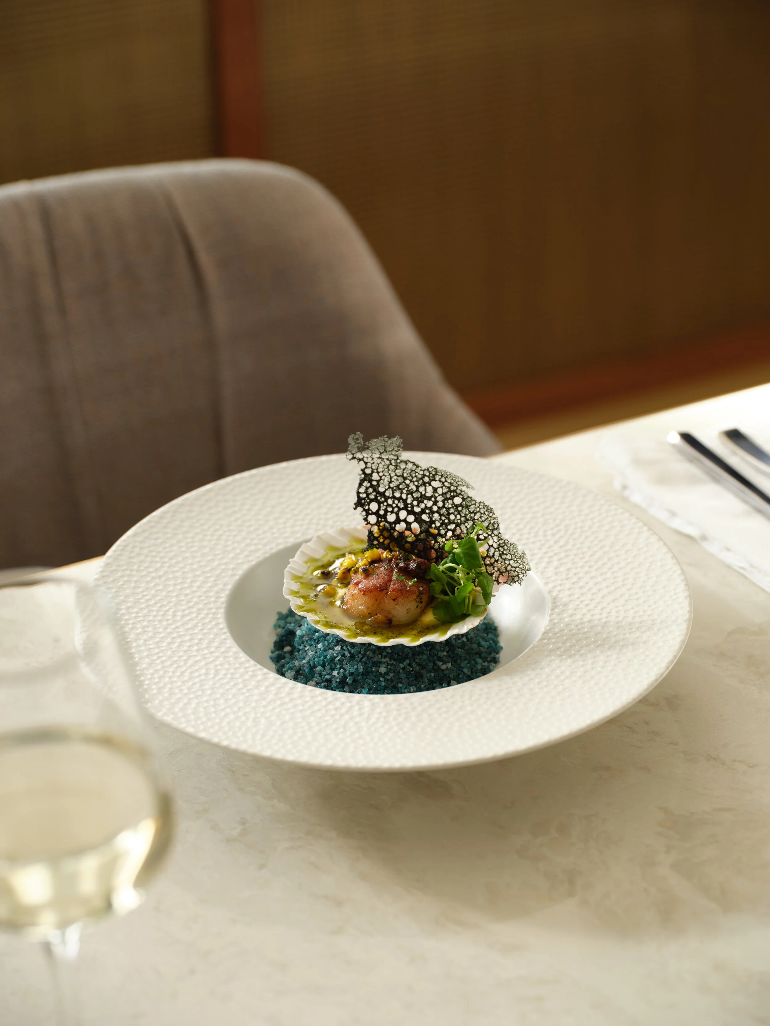 Elegant plated dish with shell, microgreens and edible black lace garnish on a white plate.