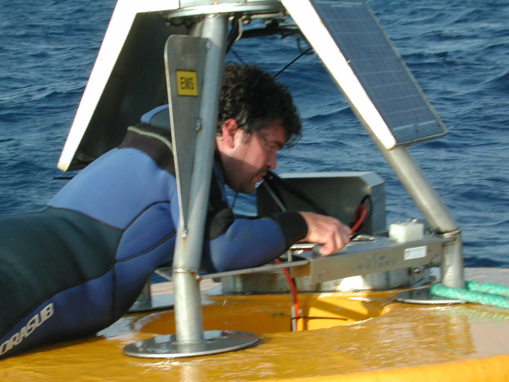 A man working on equipment on a yellow submersible, with the ocean in the background.