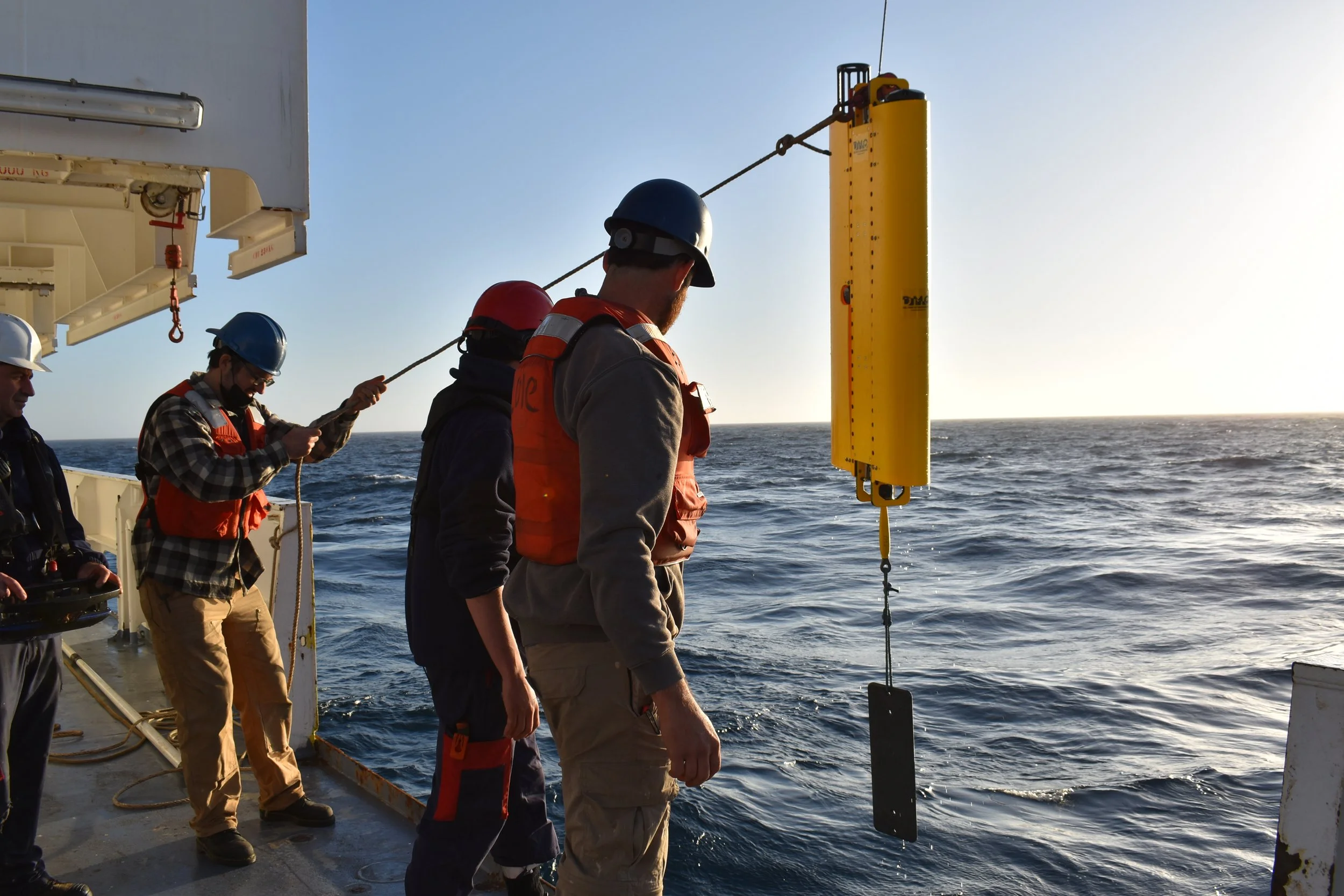 Crew members on a ship releasing a scientific instrument into the ocean water during daylight hours.
