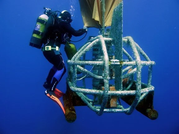 A scuba diver examining a large, underwater metallic structure.