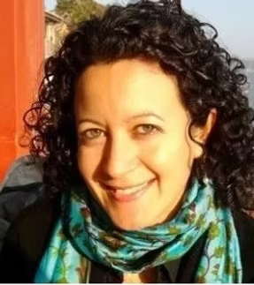 A woman with curly dark hair smiling outdoors, wearing a colorful scarf.