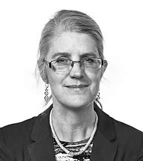 Black and white portrait of a woman with glasses, gray hair, wearing a blazer and necklace.