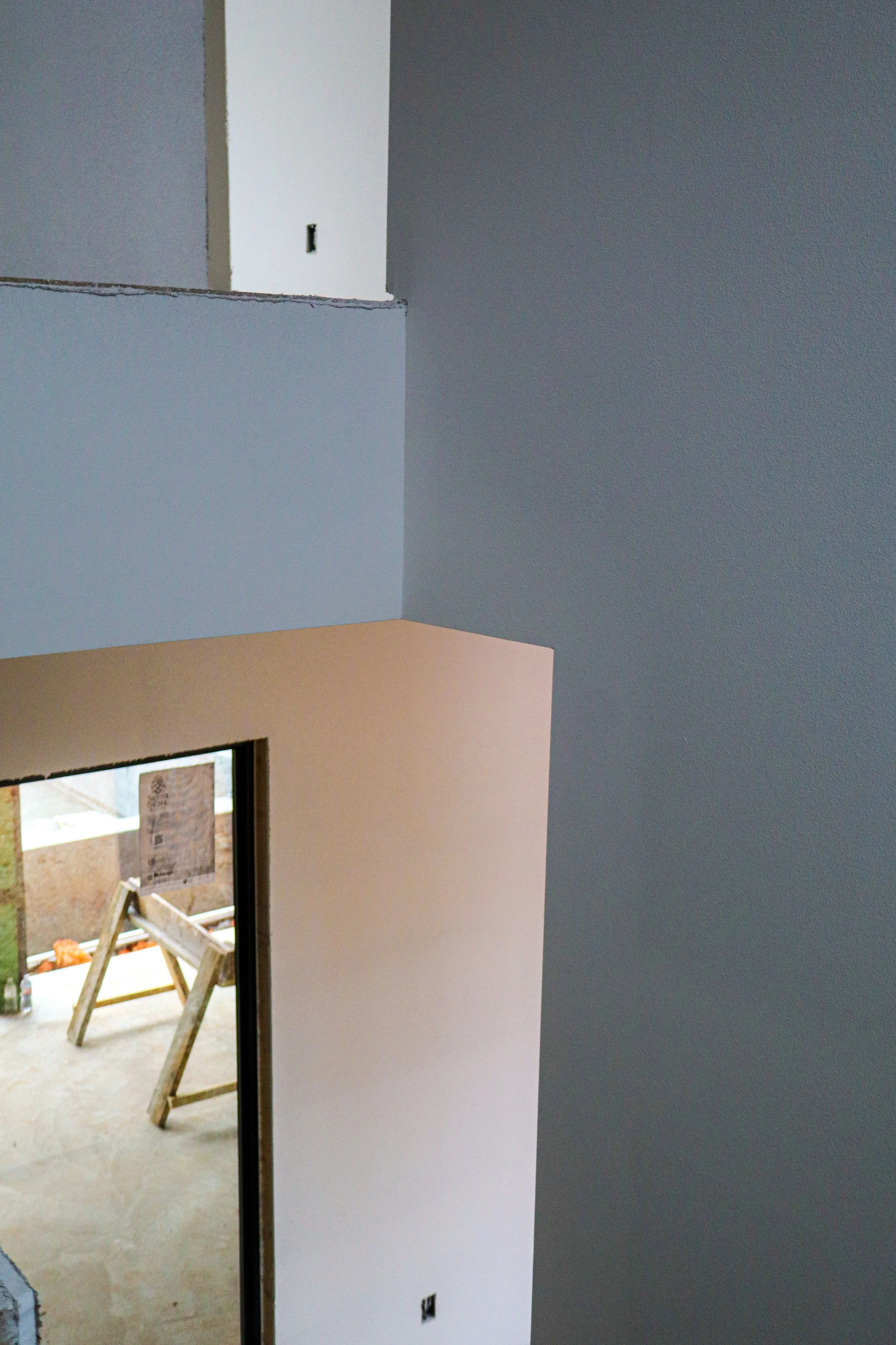 Interior of a house under construction, showing painted walls, a doorway, and a window with construction materials outside.