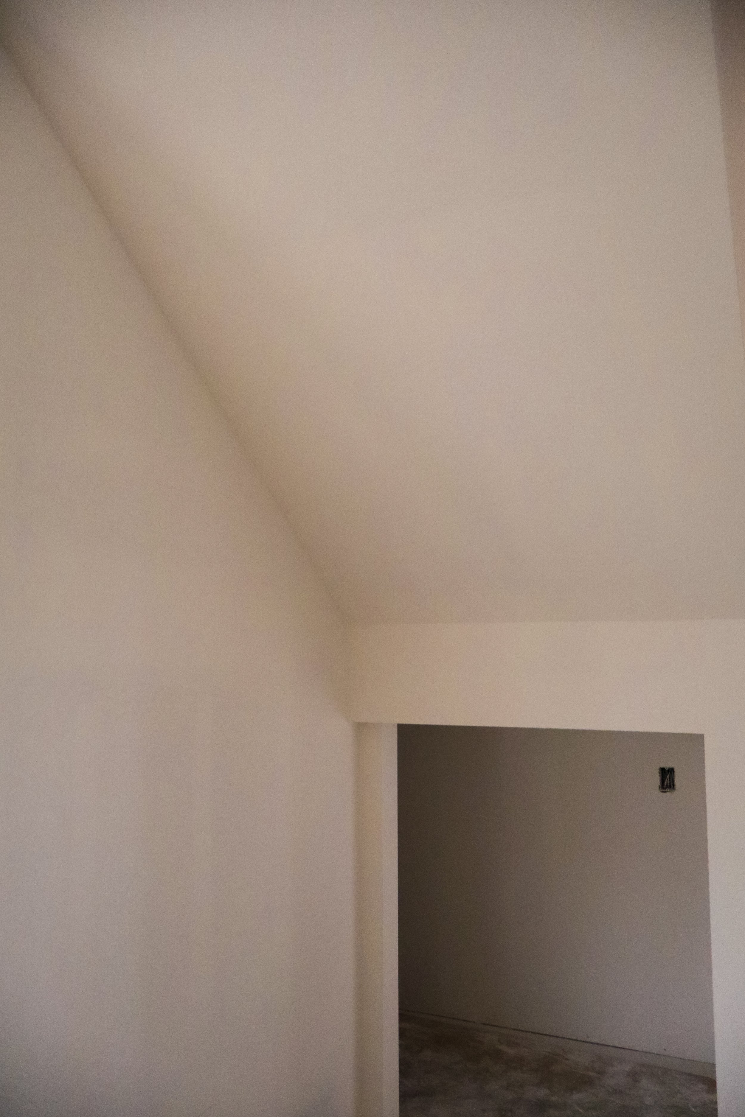 Interior view of a room under construction with white walls, a doorway, and an exposed electrical outlet.