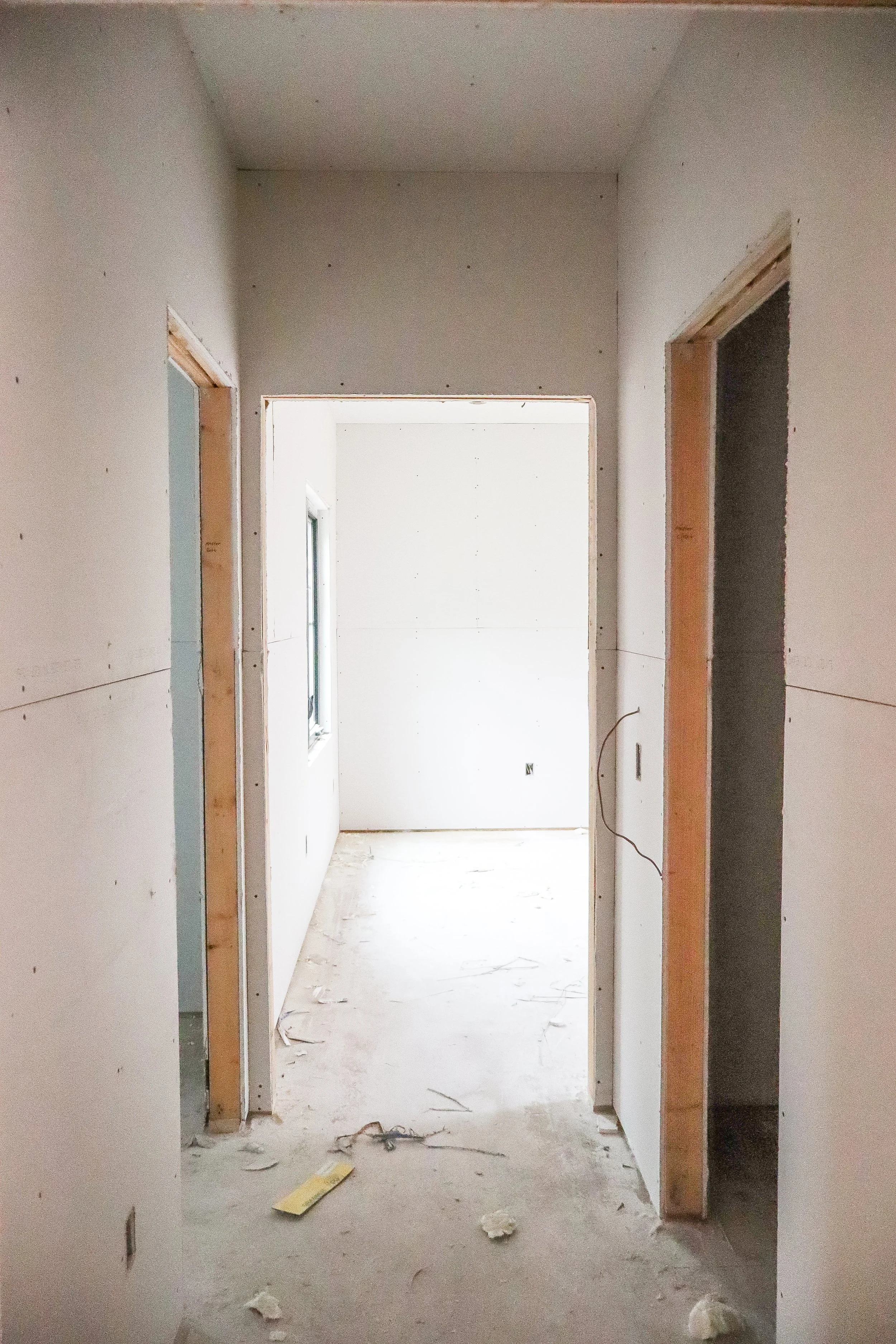 Interior view of a house under construction, showing unfinished wall drywall and door frames, with debris on the floor.