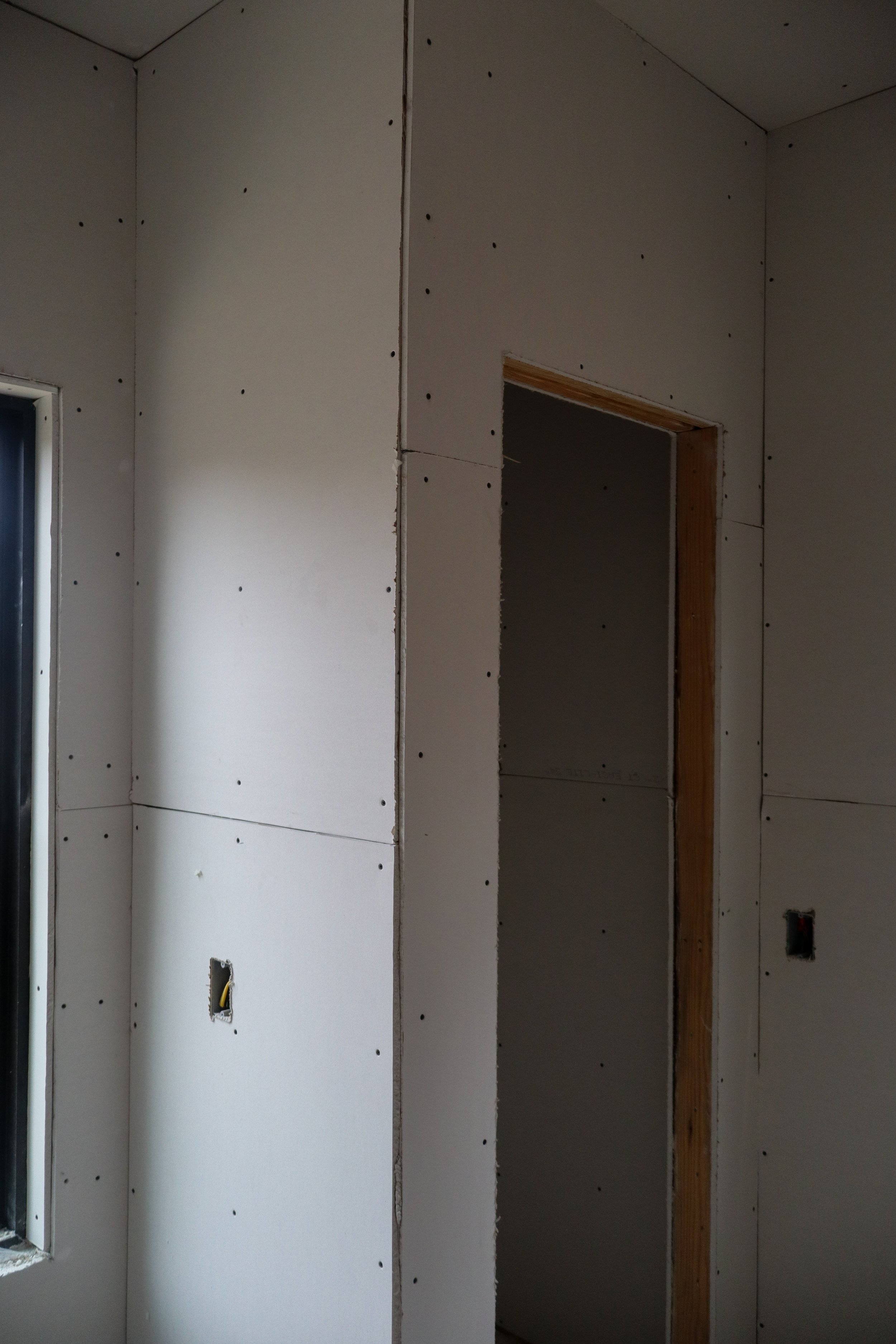 Interior wall under construction with drywall panels, Electrical outlets, and framing.