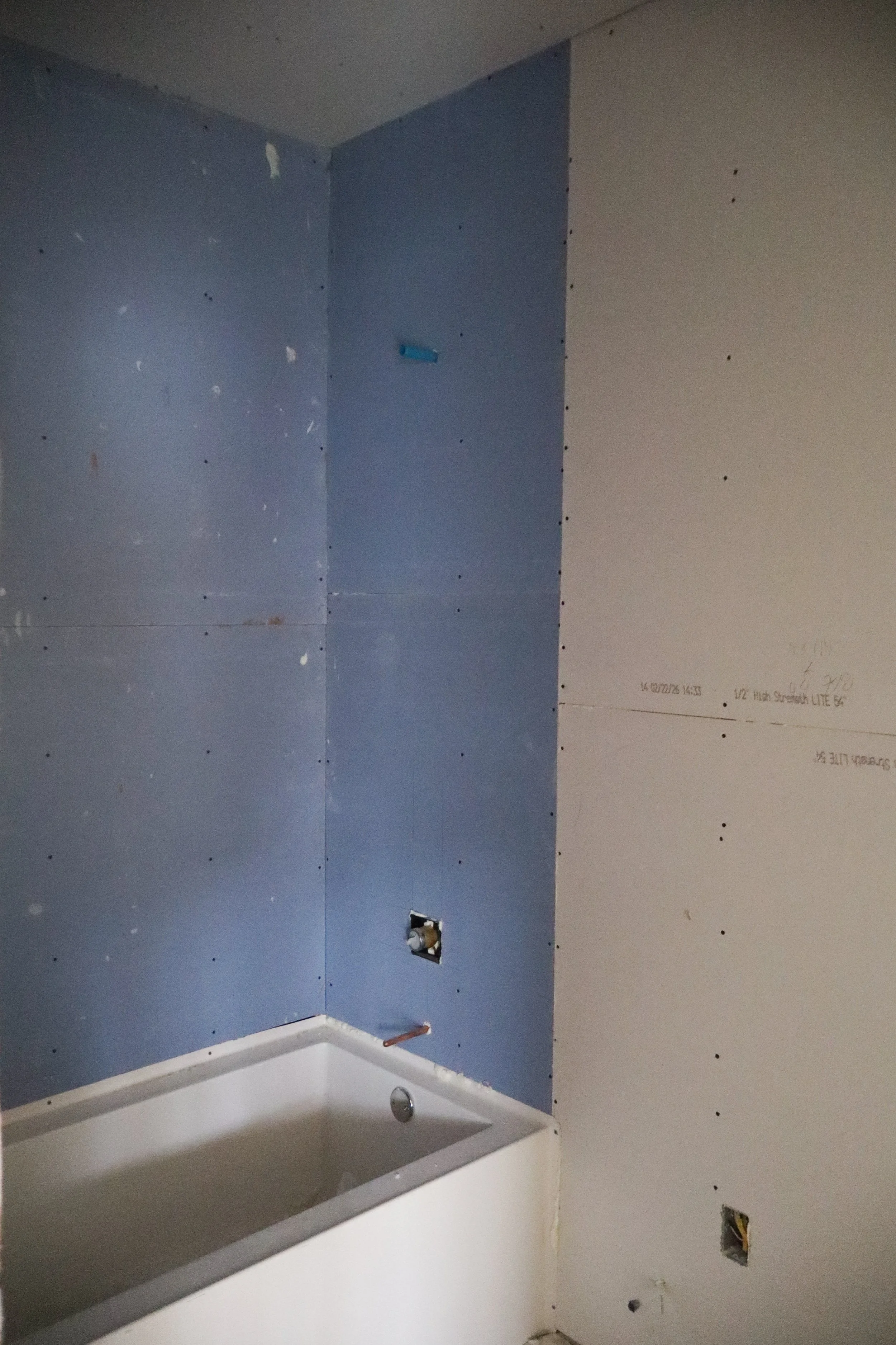 Bathroom under renovation with drywall installed on walls and a bathtub in the corner.