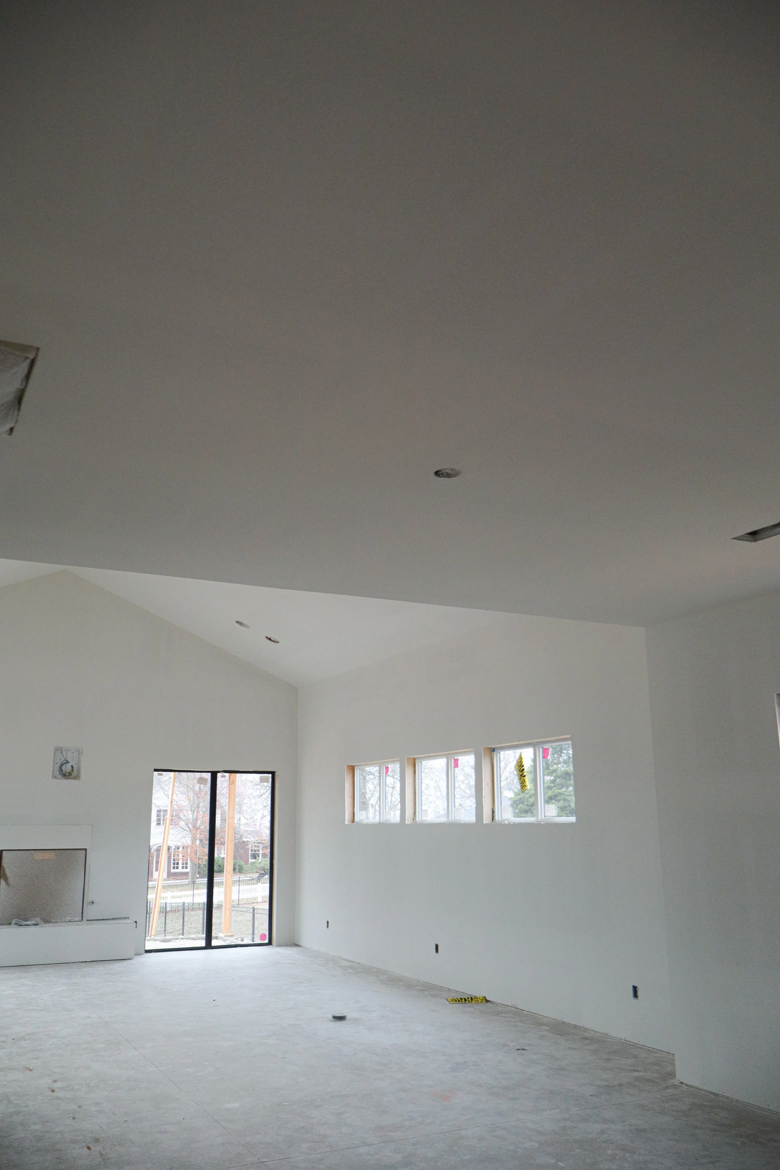 Interior of a house under construction with white walls, multiple windows, and a sliding glass door leading outside.