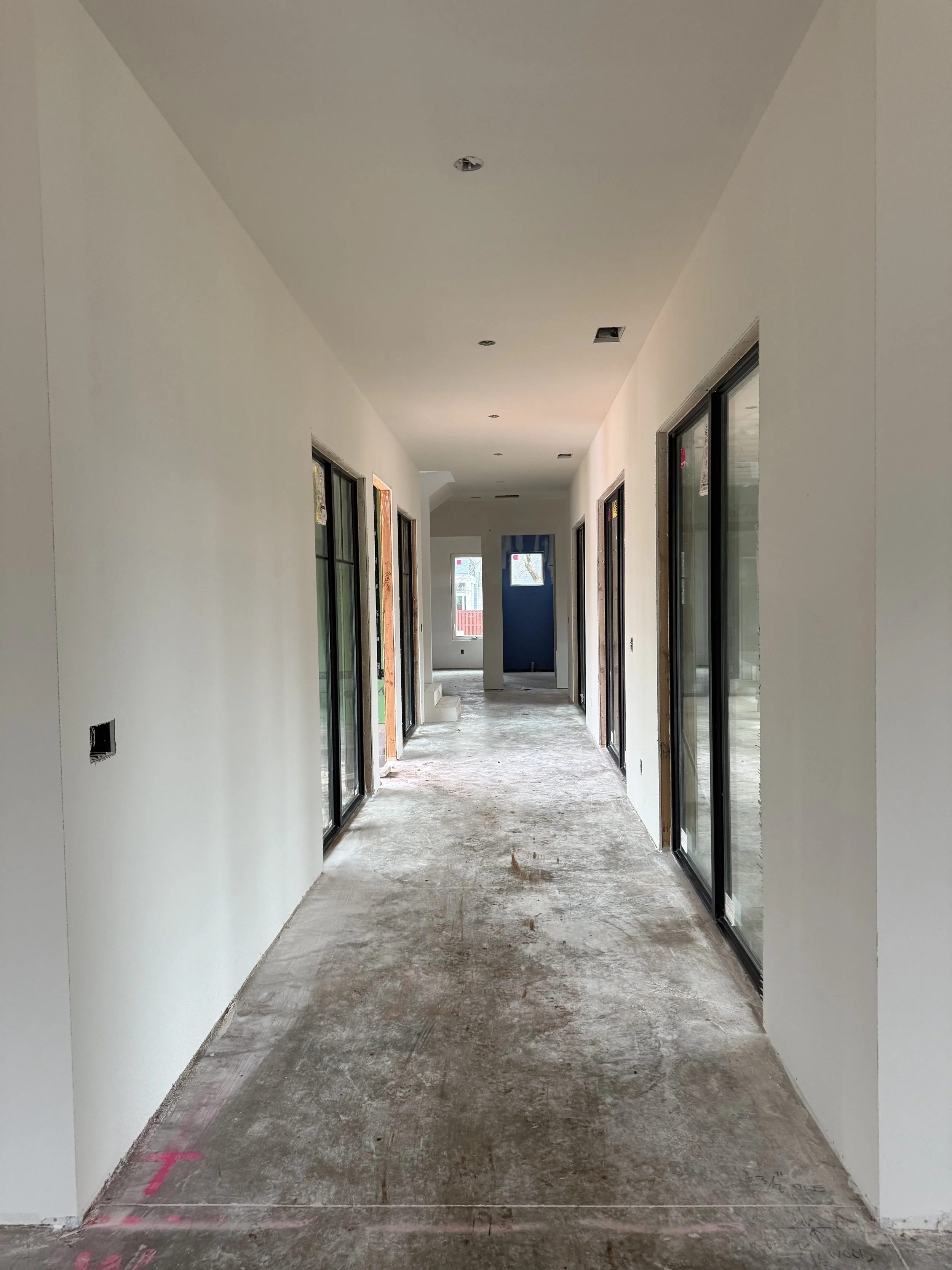 Empty hallway inside a building under construction with sliding glass doors on either side and new drywall walls.