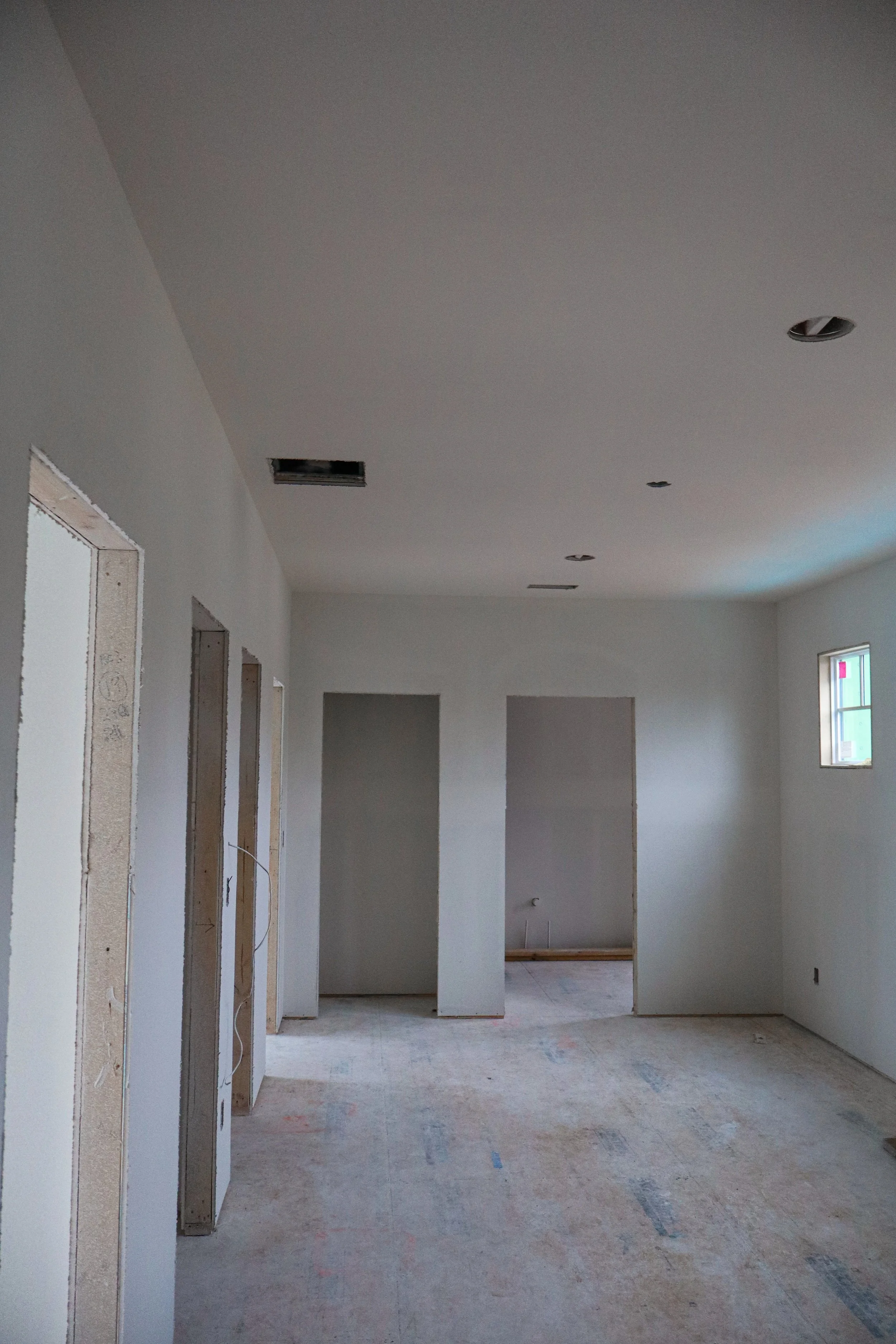 Empty room under construction with unfinished walls, ceiling openings for lights, and a small window.