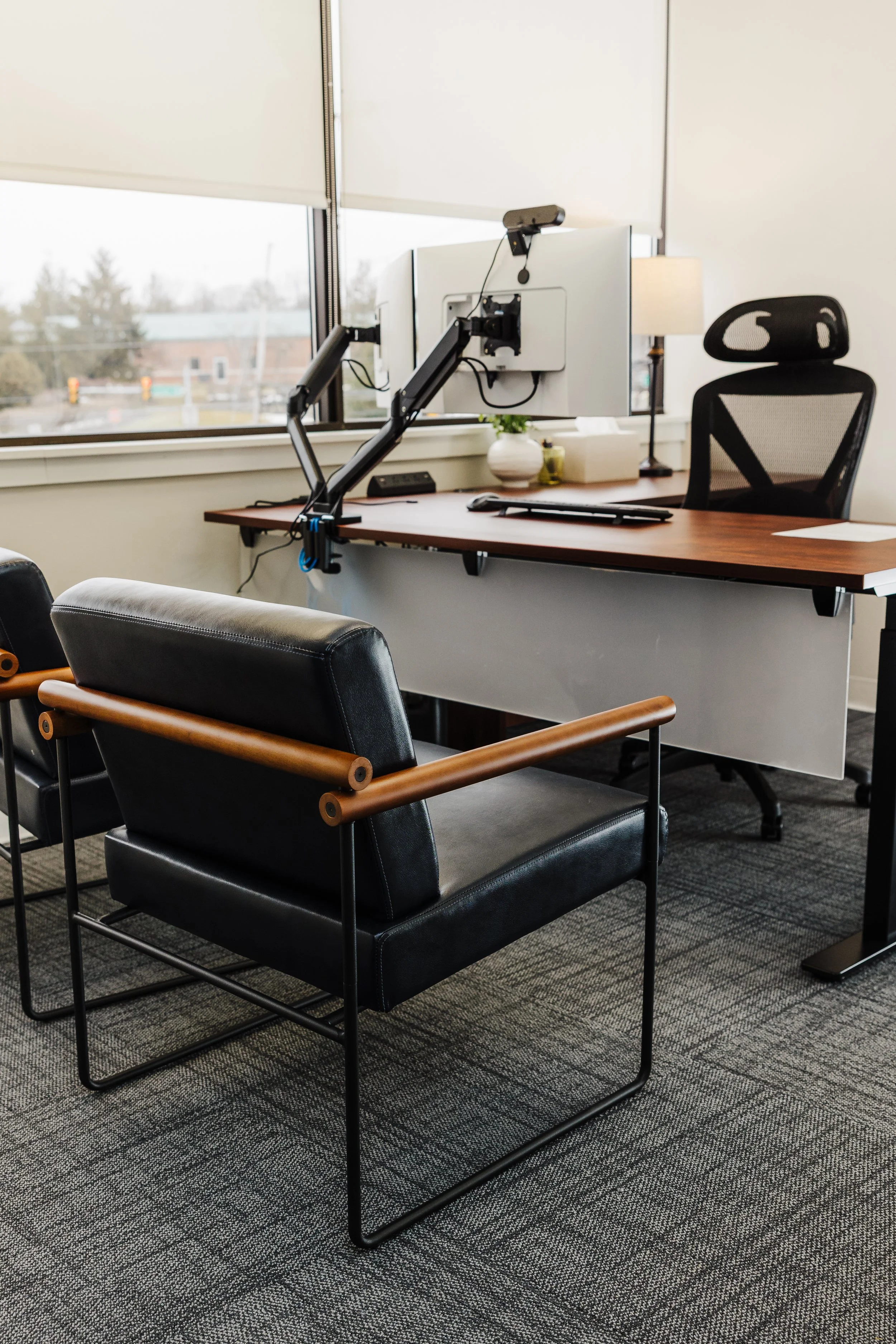 Office space with a desk, black mesh ergonomic chair, and a high-tech eye-testing device attached to the desk, near a window.