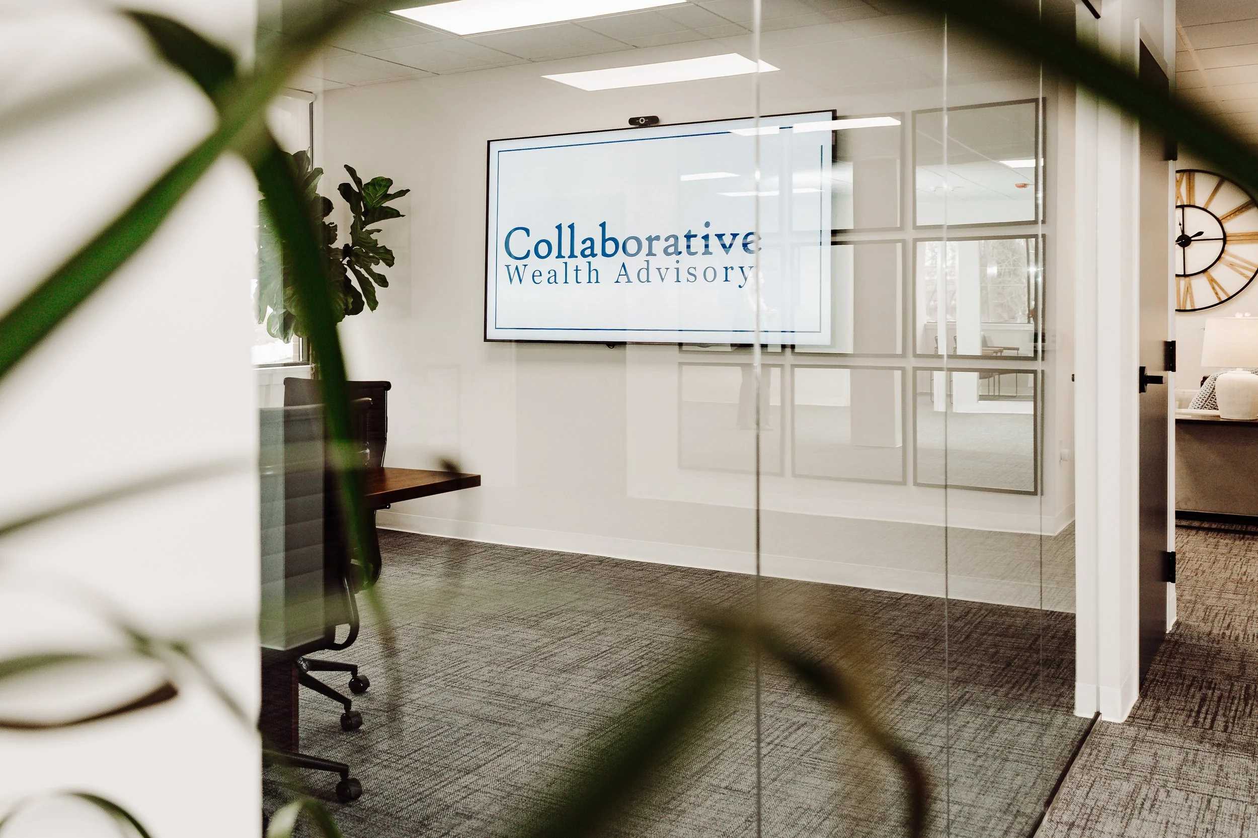 Office conference room with a large digital screen displaying "Collaborative Wealth Advisory" and a glass door with grid design, part of a modern and professional workspace.