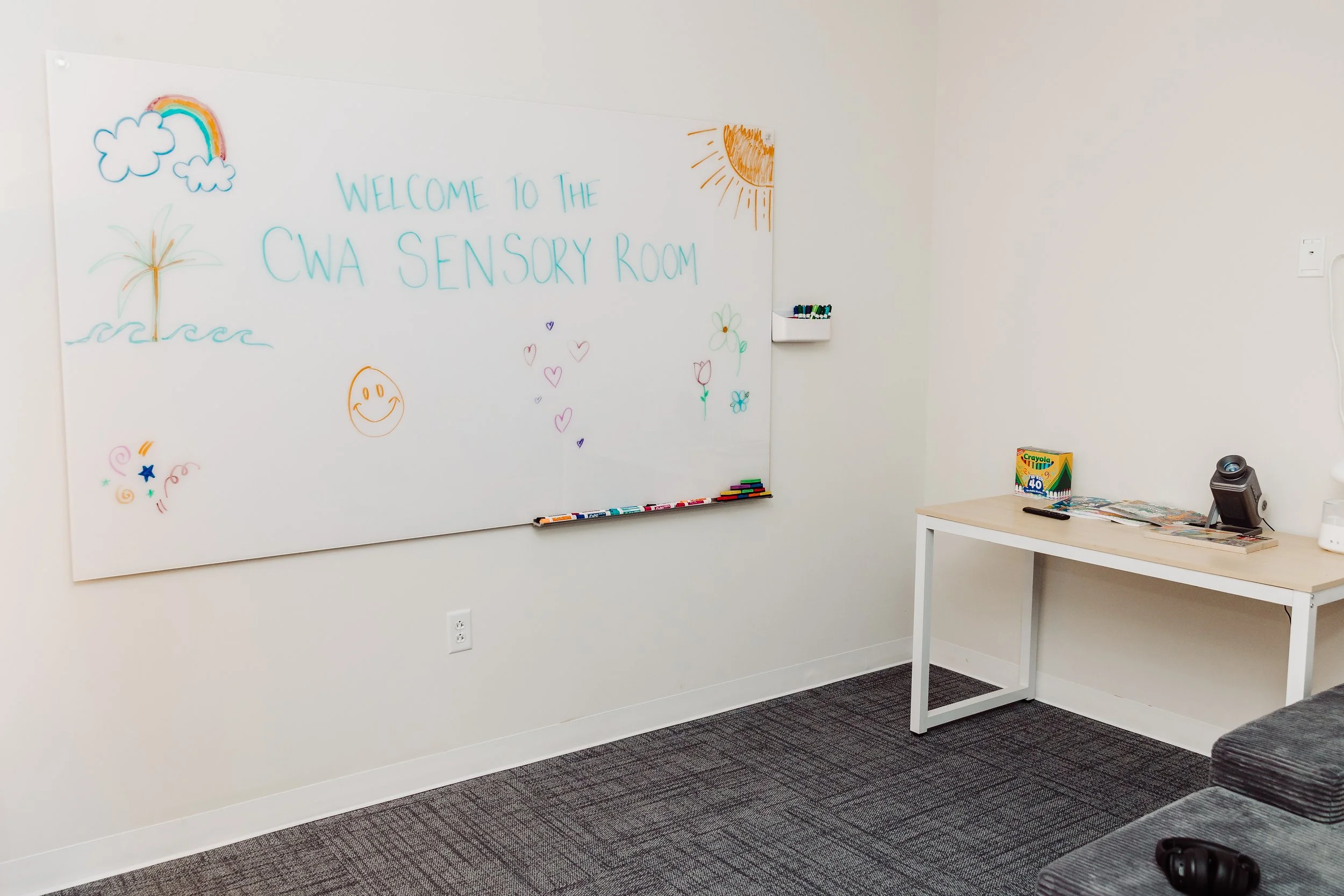 Whiteboard with colorful drawings and writing, reading 'Welcome to the CWA Sensory Room'.
