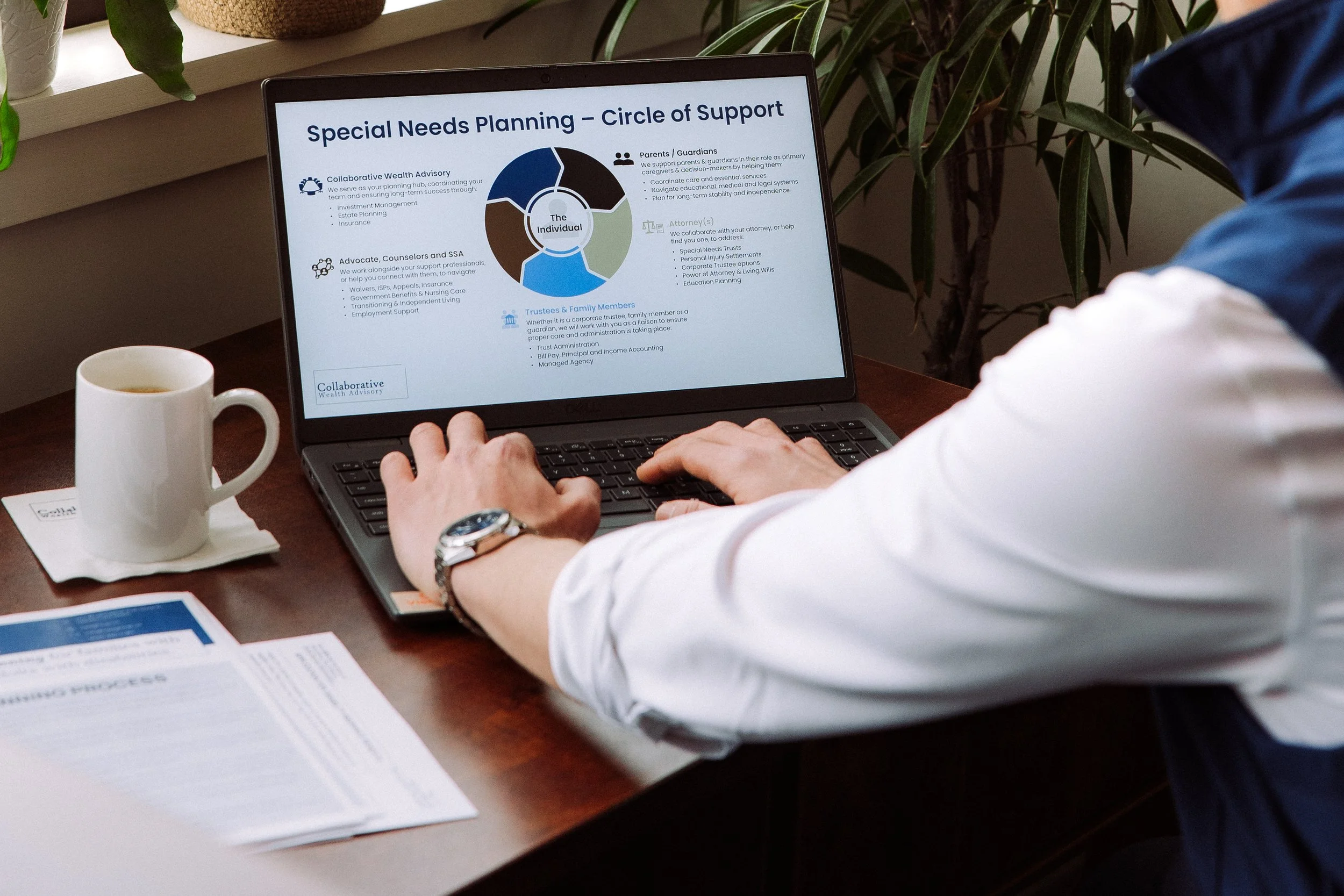 Person working on a laptop with a presentation titled 'Special Needs Planning - Circle of Support,' a coffee mug on a saucer, papers, and a plant nearby.