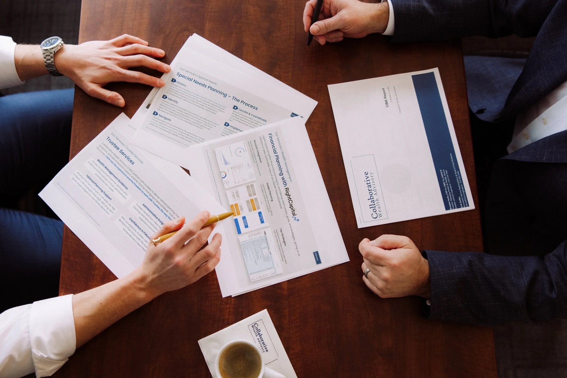 Two people sitting at a wooden table with documents, brochures, and a cup of coffee, discussing financial planning and special needs planning.