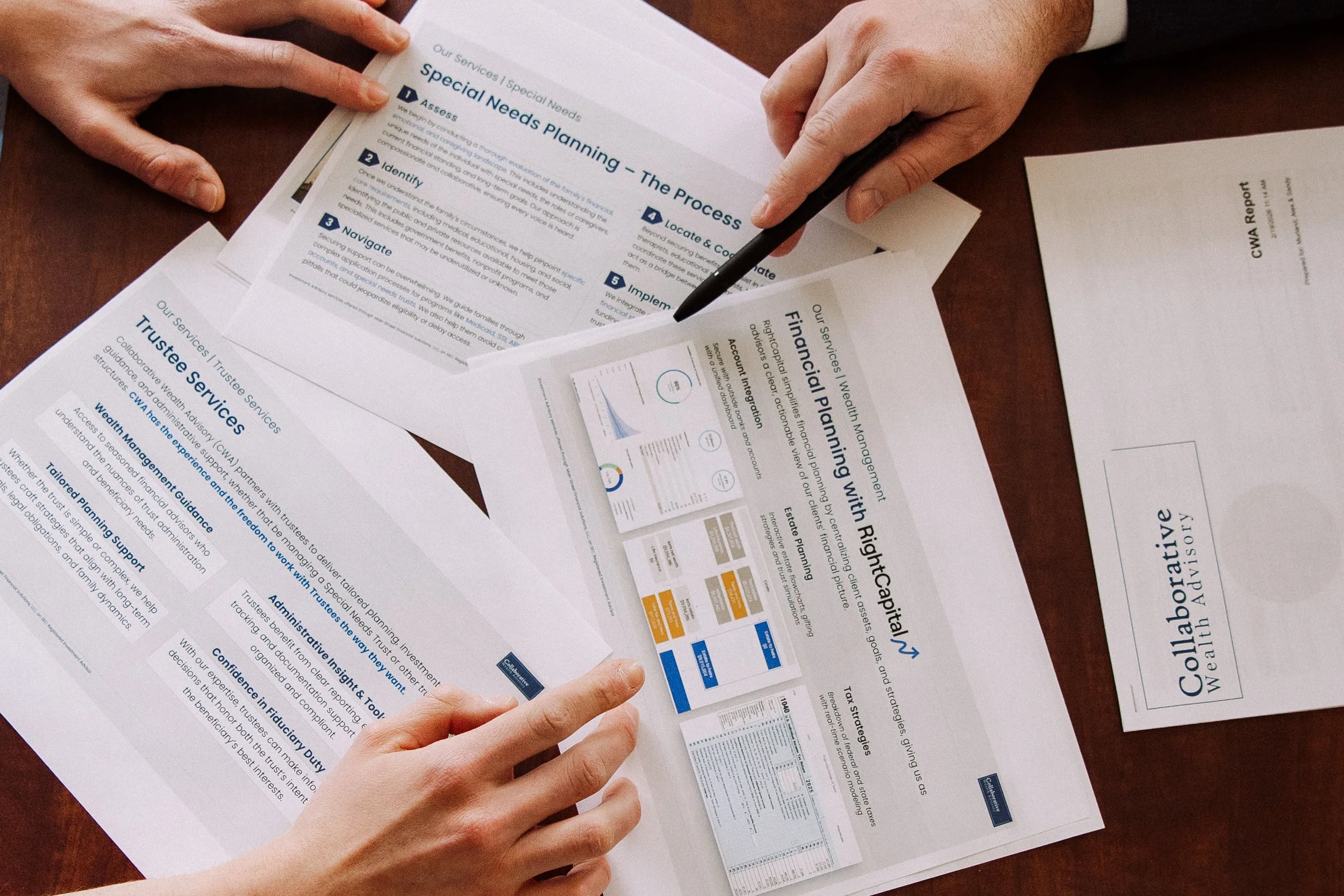 Two people reviewing documents on a wooden table, including reports on special needs planning and wealth management, with one person pointing at the documents with a pen.