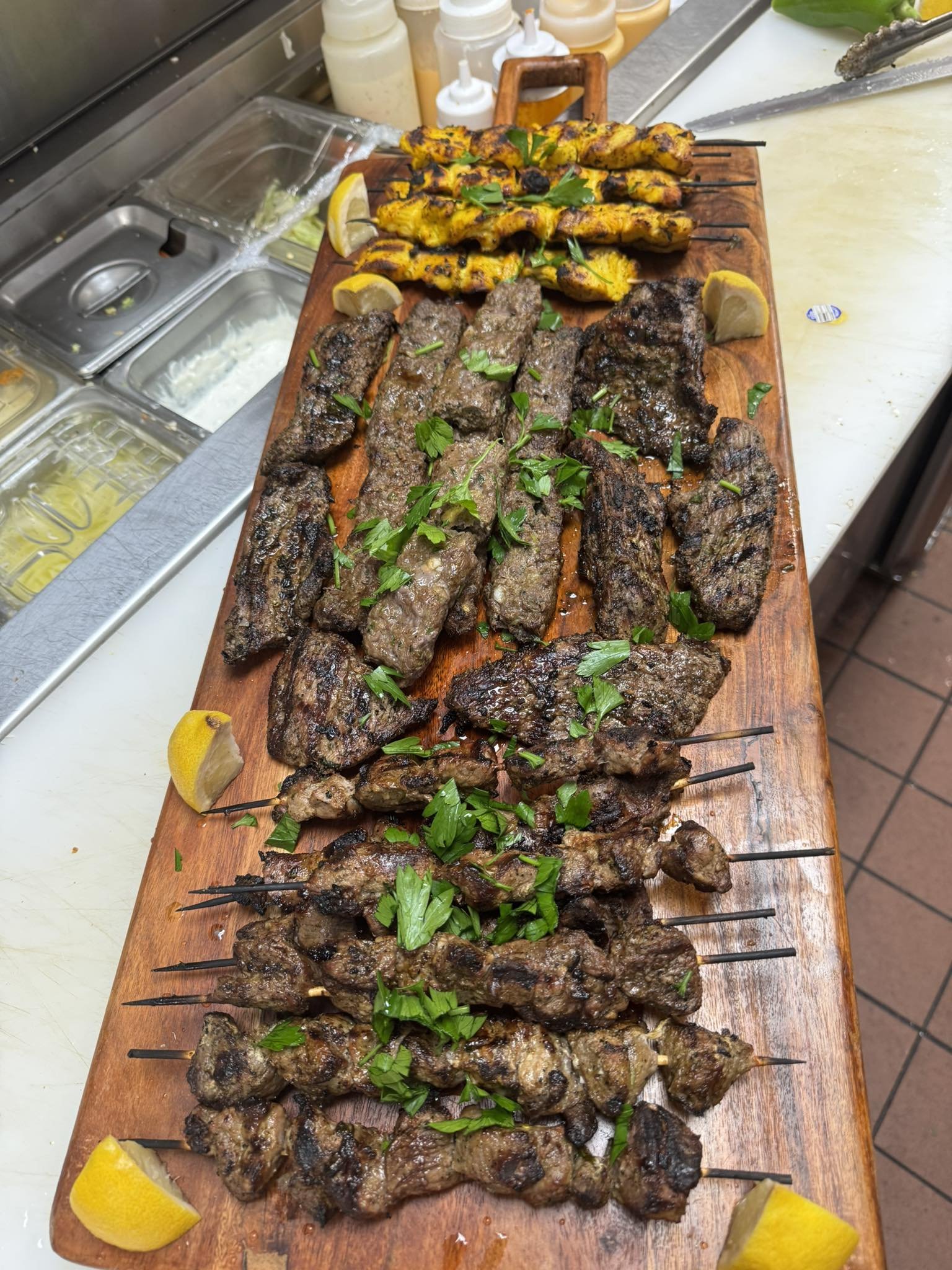Assorted grilled skewers of meat and vegetables garnished with parsley and lemon wedges on a wooden platter.