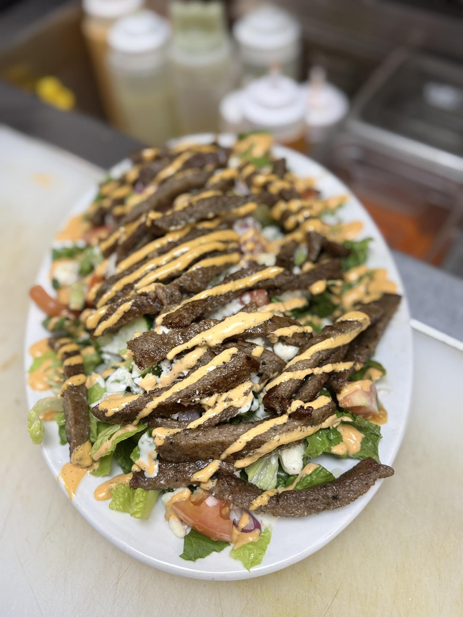 A plate of beef fajita salad topped with grilled beef strips, drizzled with creamy dressing, on a bed of lettuce, tomatoes, and cheese.
